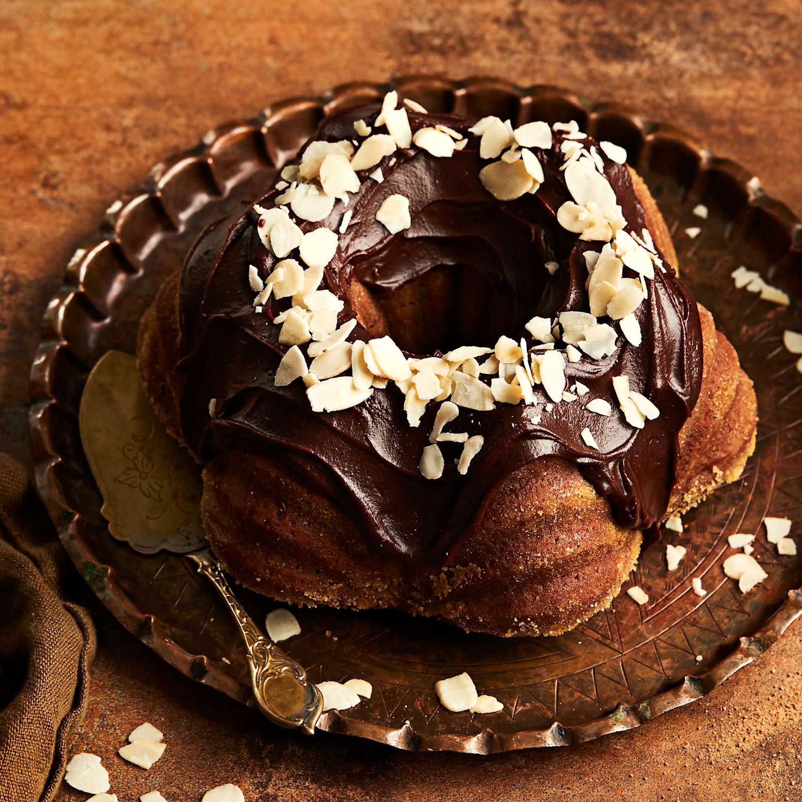 Arabialainen maustekakku mantelilastuilla koristeltuna. Vieressä teepannu, ruskea liina ja kanelitankoja.