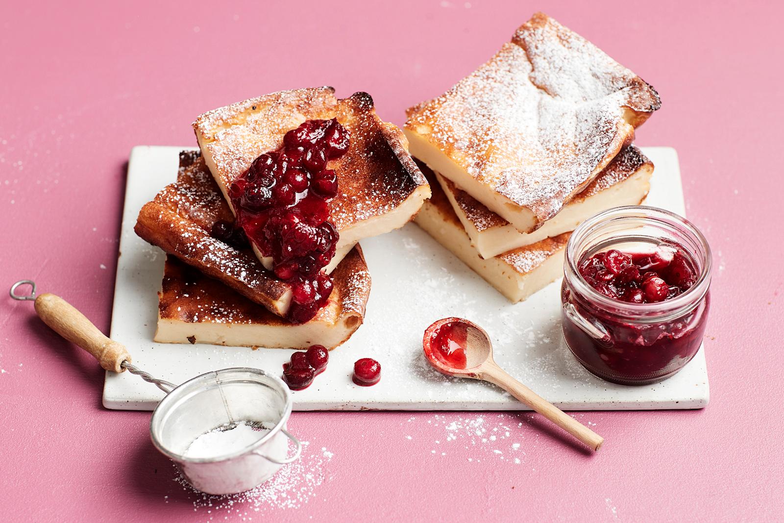 Rahkapannari ja karpalosose valkoisella tarjoilulautasella. Vieressä tomusokeria siivilässä, pieni puulusikka ja karpalososetta purkissa.