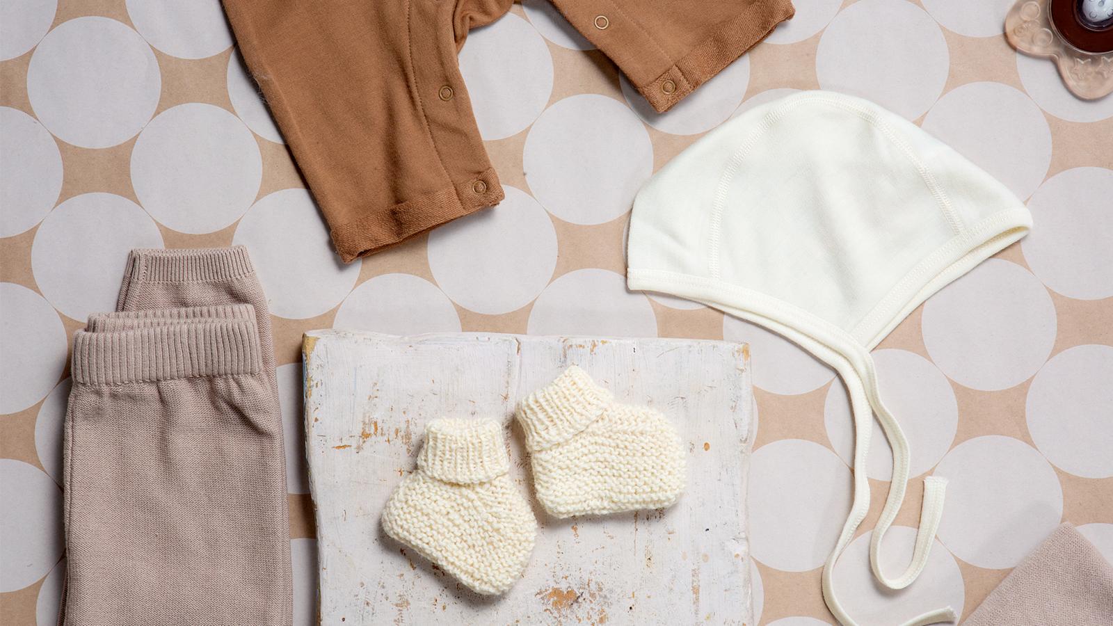 Valkoiset vauvan tossut, joiden ympärillä vauvan vaatteita.