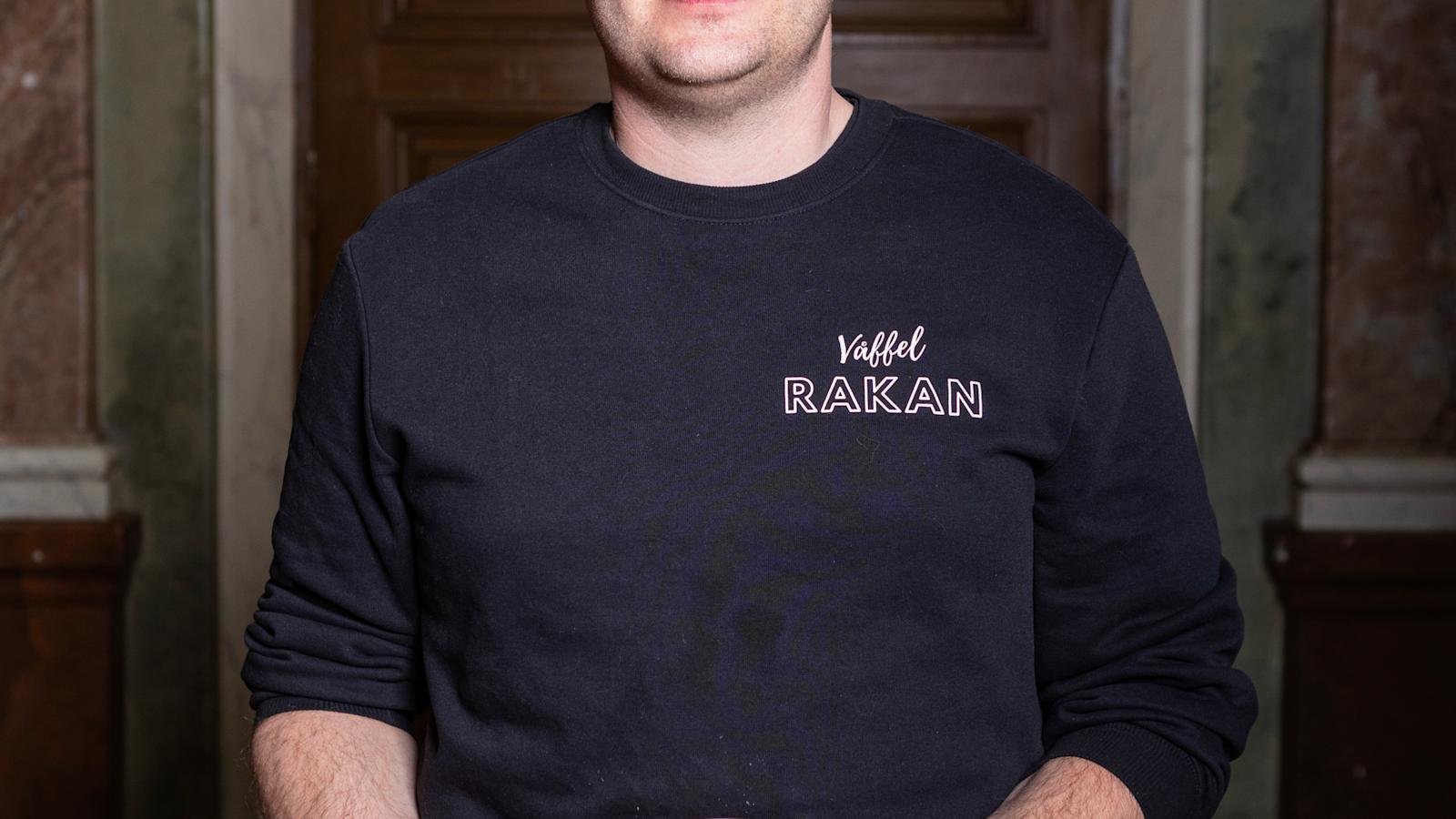 Jack Mattssonilla on käärinyt hihat mustasta paidastaan. Oikeassa kädessään hän pitelee kolmea sipulia. Vasemmassa kädessä puolestaan on lautanen, jolla on useammalla täytteellä kuorrutettu vohveli.