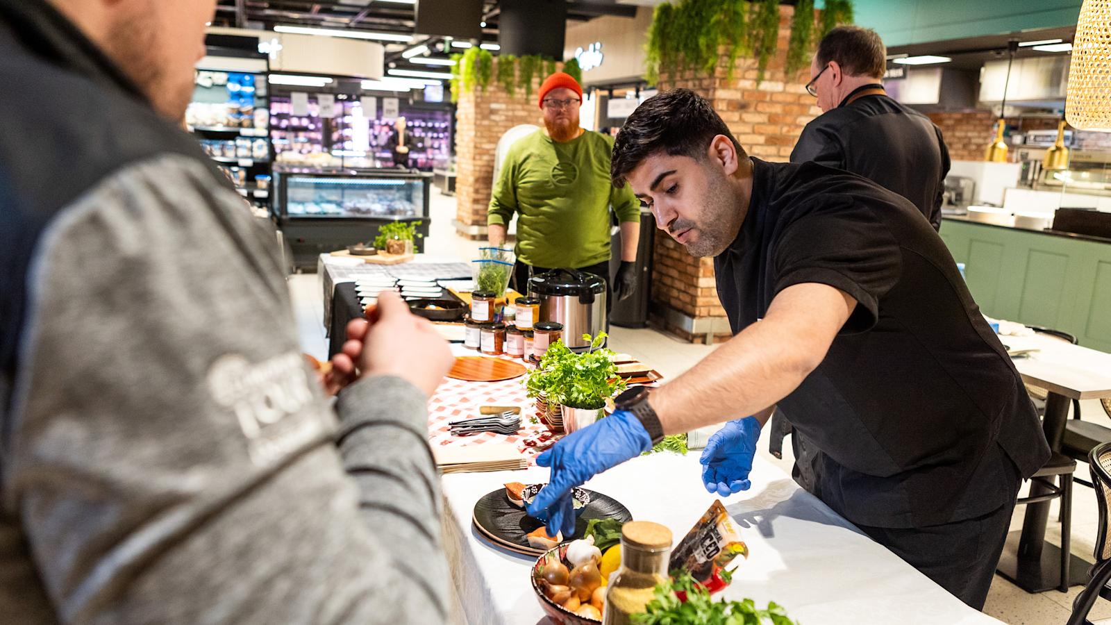 Siva Parlar maistattaa tuotteitaan kuluttajilla Suomalainen menestysresepti 2024 -kilpailun semifinaalissa. Taustalla toinen semifinalisti Roy Norro.