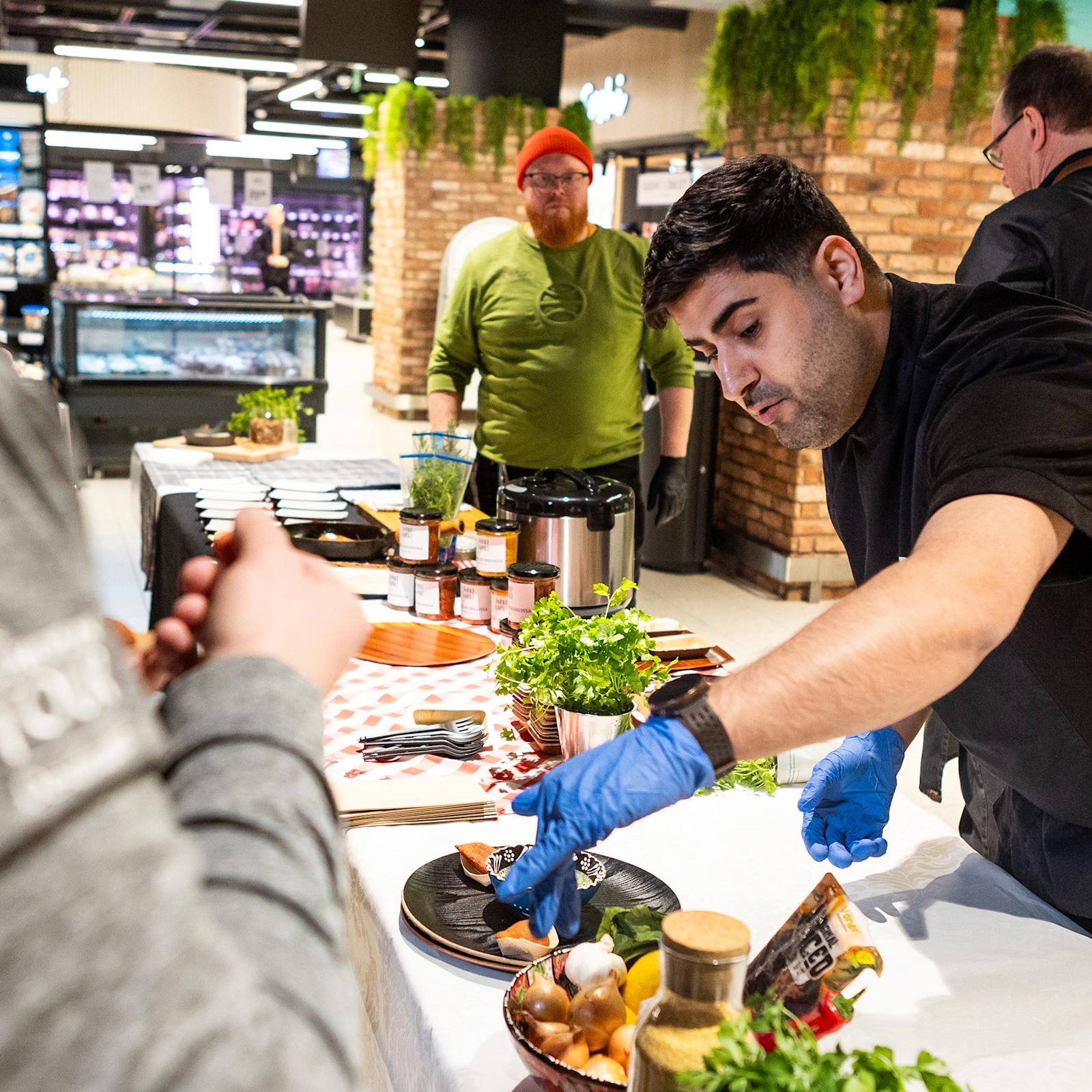 Siva Parlar maistattaa tuotteitaan kuluttajilla Suomalainen menestysresepti 2024 -kilpailun semifinaalissa. Taustalla toinen semifinalisti Roy Norro.