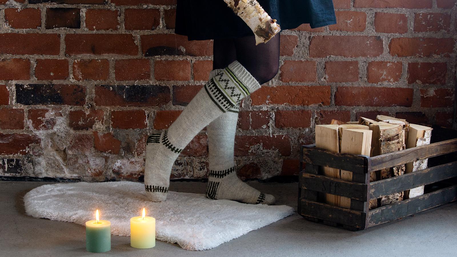 Kirjoneulesukat jalkoihin puettuna. Vieressä lattialla halkokori, kynttilöitä ja talja.