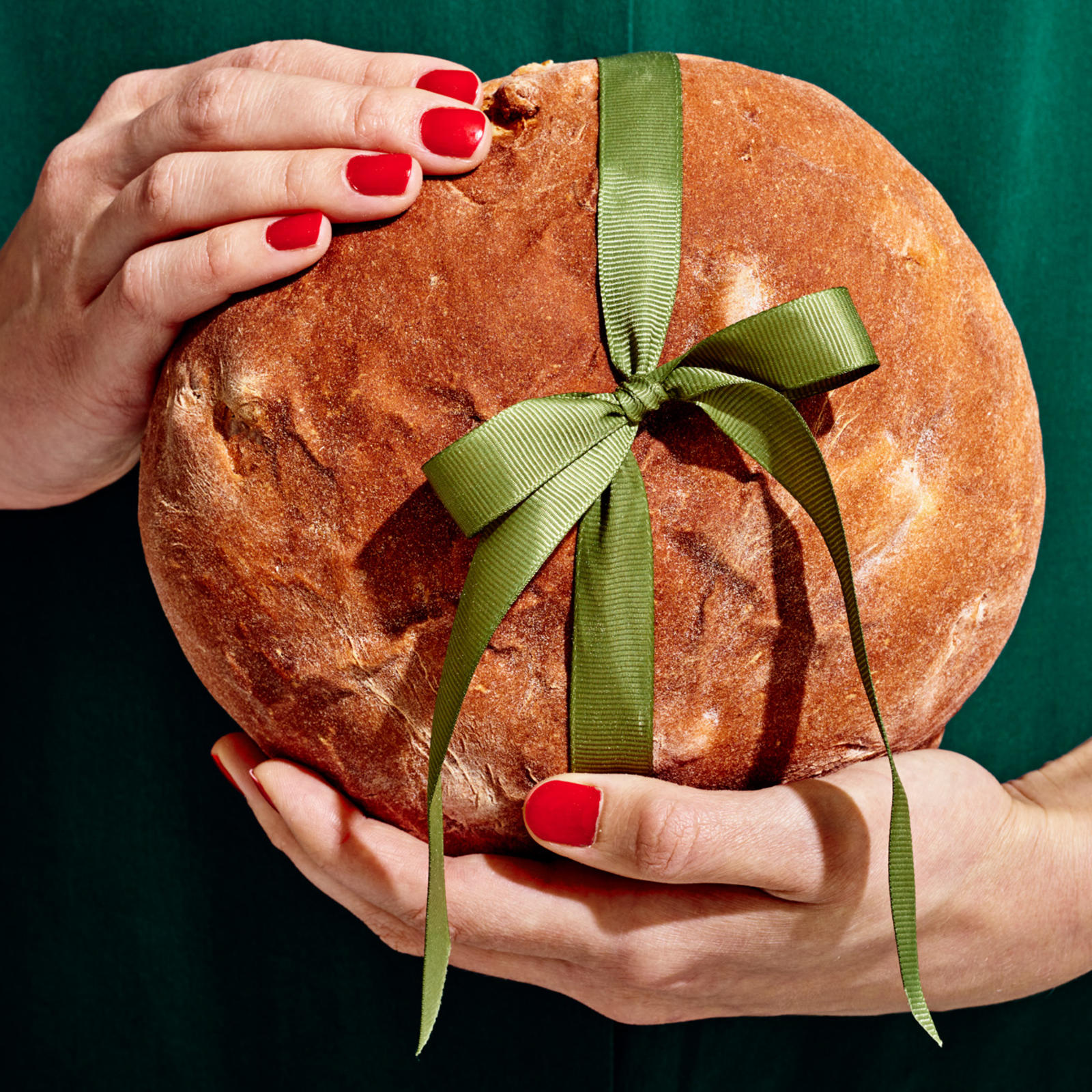 Kädet pitelevät vaaleaa joululeipää. Leivän ympärillä on vihreä rusetti.