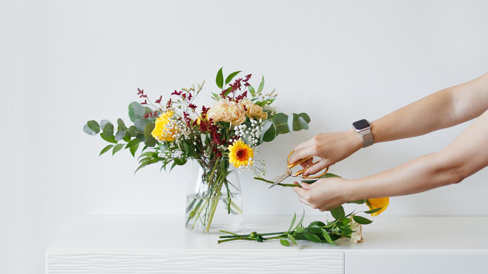 Leikkokukkakimppu ja kädet, jotka leikkaavat kukkien varsia
