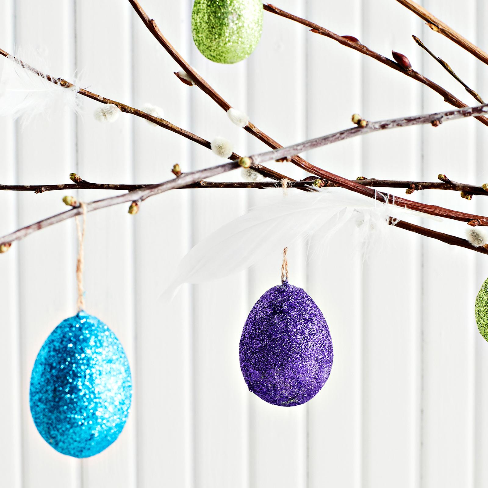 Kimallejauheella koristeltuja pääsiäismunia pajunoksiin ripustettuina.