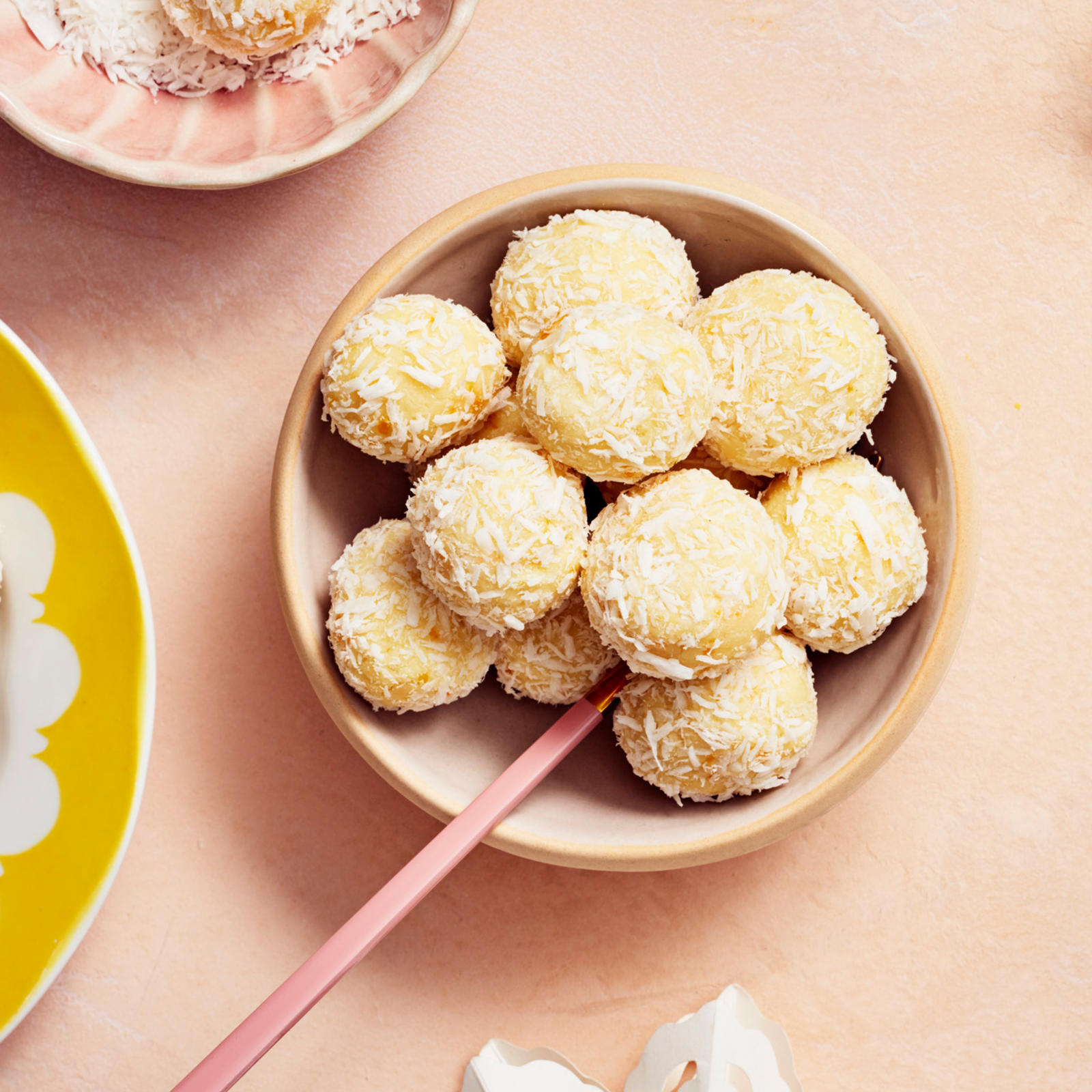 Pienessä kulhossa sekä lautasella valkosuklaatryffeleitä, jotka on päällystetty kookoshiutaleilla.