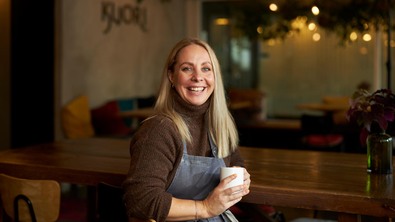Katariina Vesterinen pitää käsissään kahvikuppia ja hymyilee