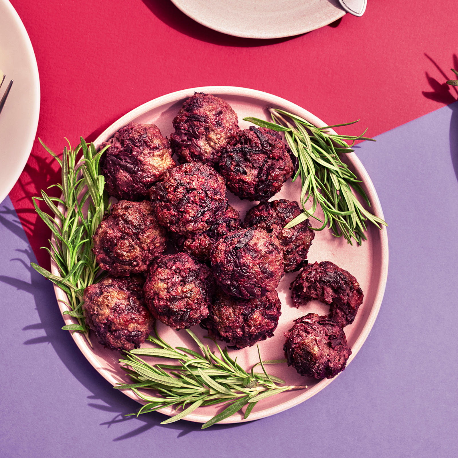 Lindströmin lihapullia lautasella rosmariinin oksilla koristeltuna. Vieressä lautanen, jossa perunamuusia, lihapullia ja haarukka sekä pienempi lautanen, jossa pelkkiä lihapullia.