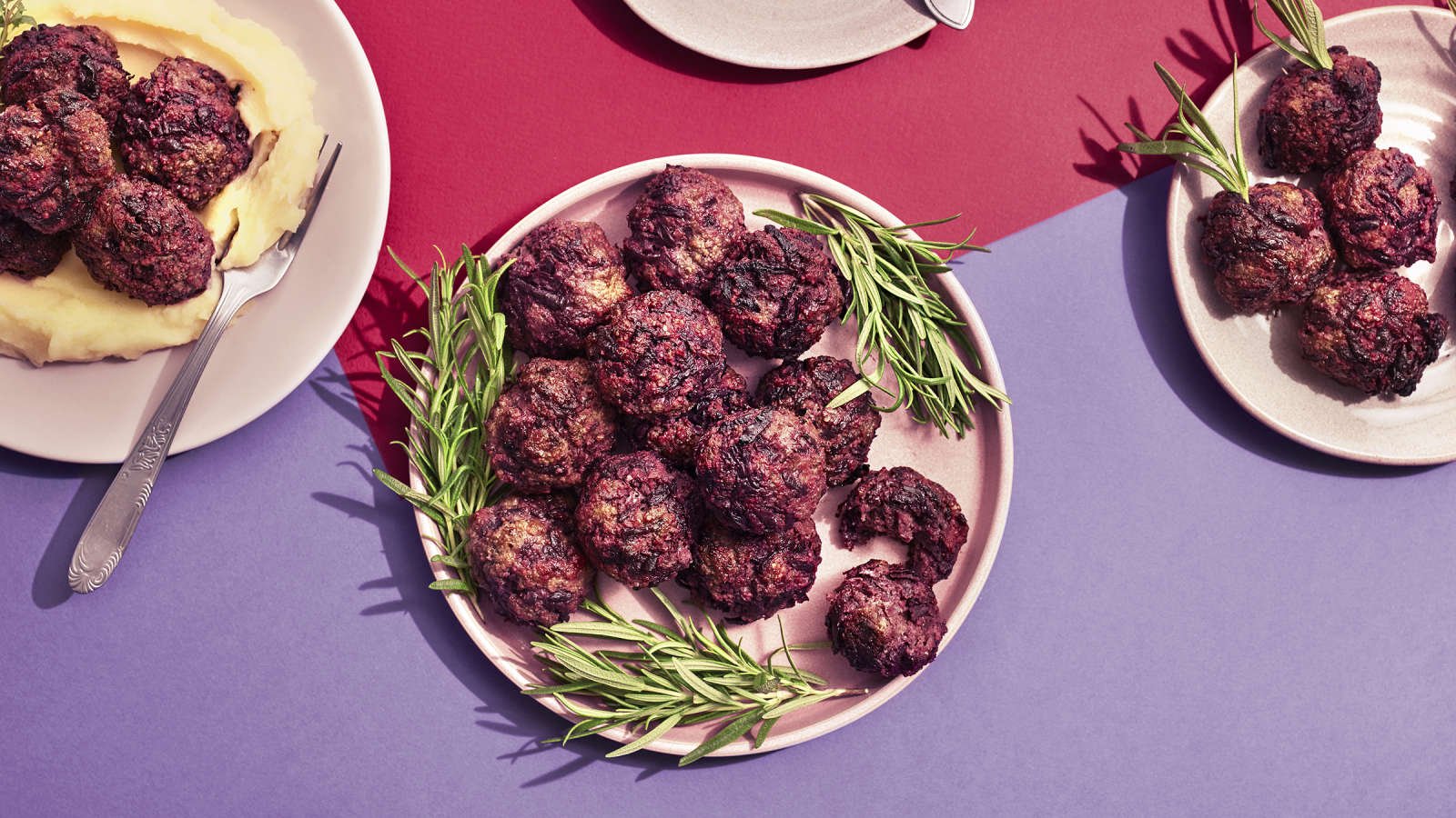 Lindströmin lihapullia lautasella rosmariinin oksilla koristeltuna. Vieressä lautanen, jossa perunamuusia, lihapullia ja haarukka sekä pienempi lautanen, jossa pelkkiä lihapullia.