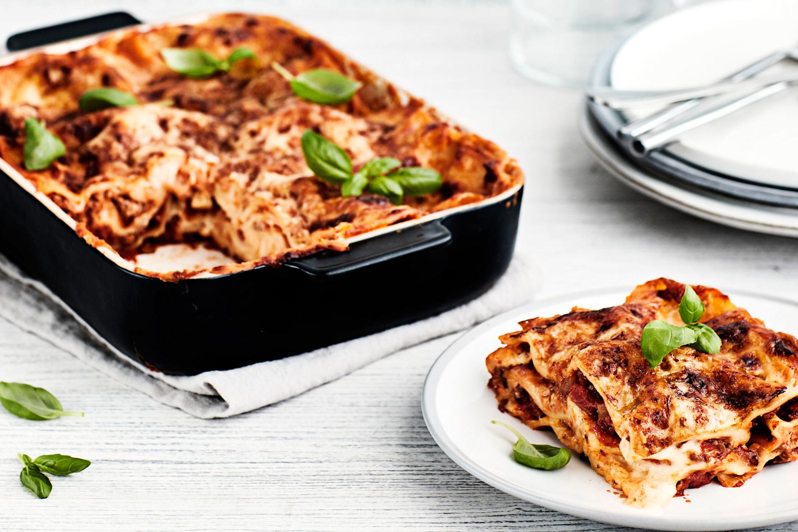 Lasagne mustassa uunivuoassa ja lautanen, jonka päällä basilikan lehdillä koristeltu annos lasagnea.