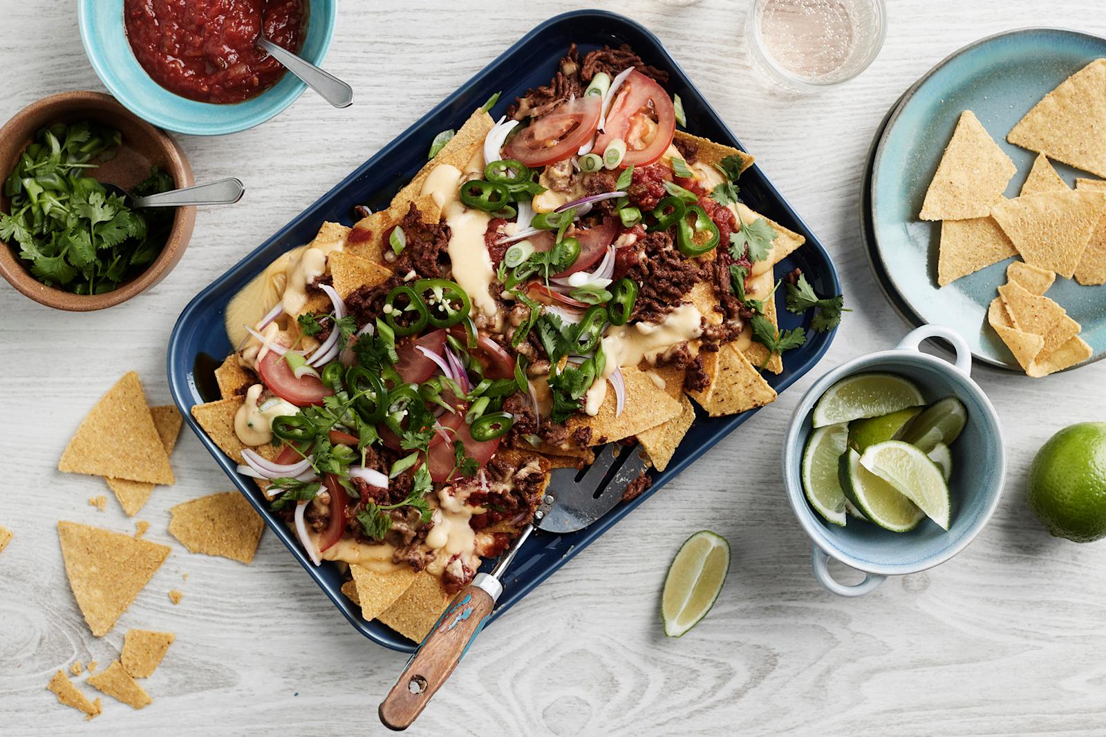 Nachopelti, jonka ympärillä tortillalastuja, limeviipaleita, korianteria ja salsakastiketta omissa kupeissaan.