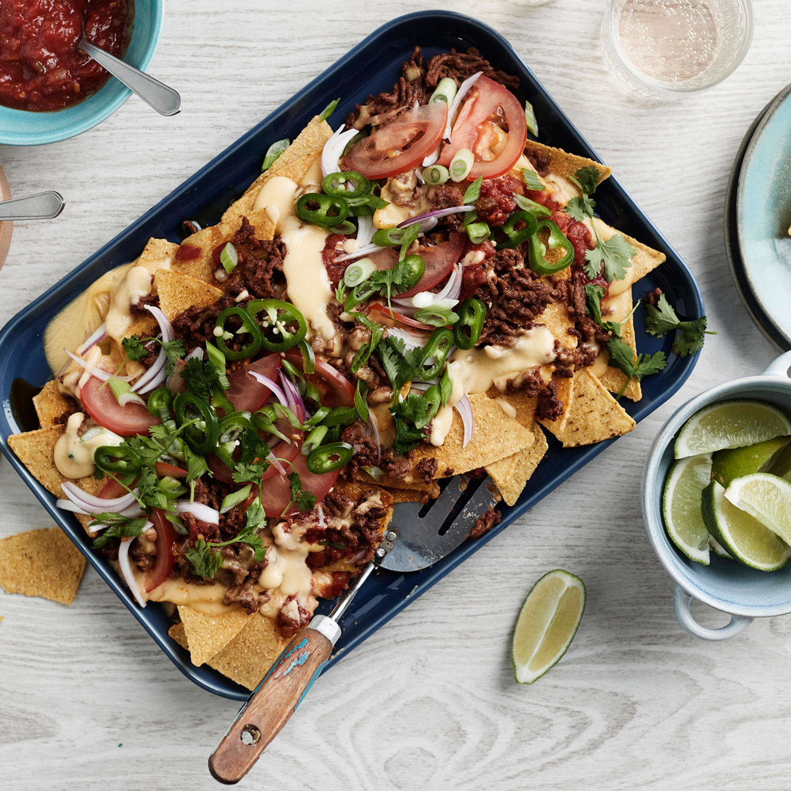 Nachopelti, jonka ympärillä tortillalastuja, limeviipaleita, korianteria ja salsakastiketta omissa kupeissaan.