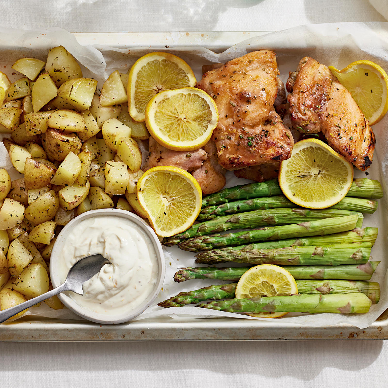 Appelsiini-kanapelti, jossa broilerin paistileikkeitä, perunoita ja tankoparsaa sekä pienessä kulhossa jogurttikastiketta.