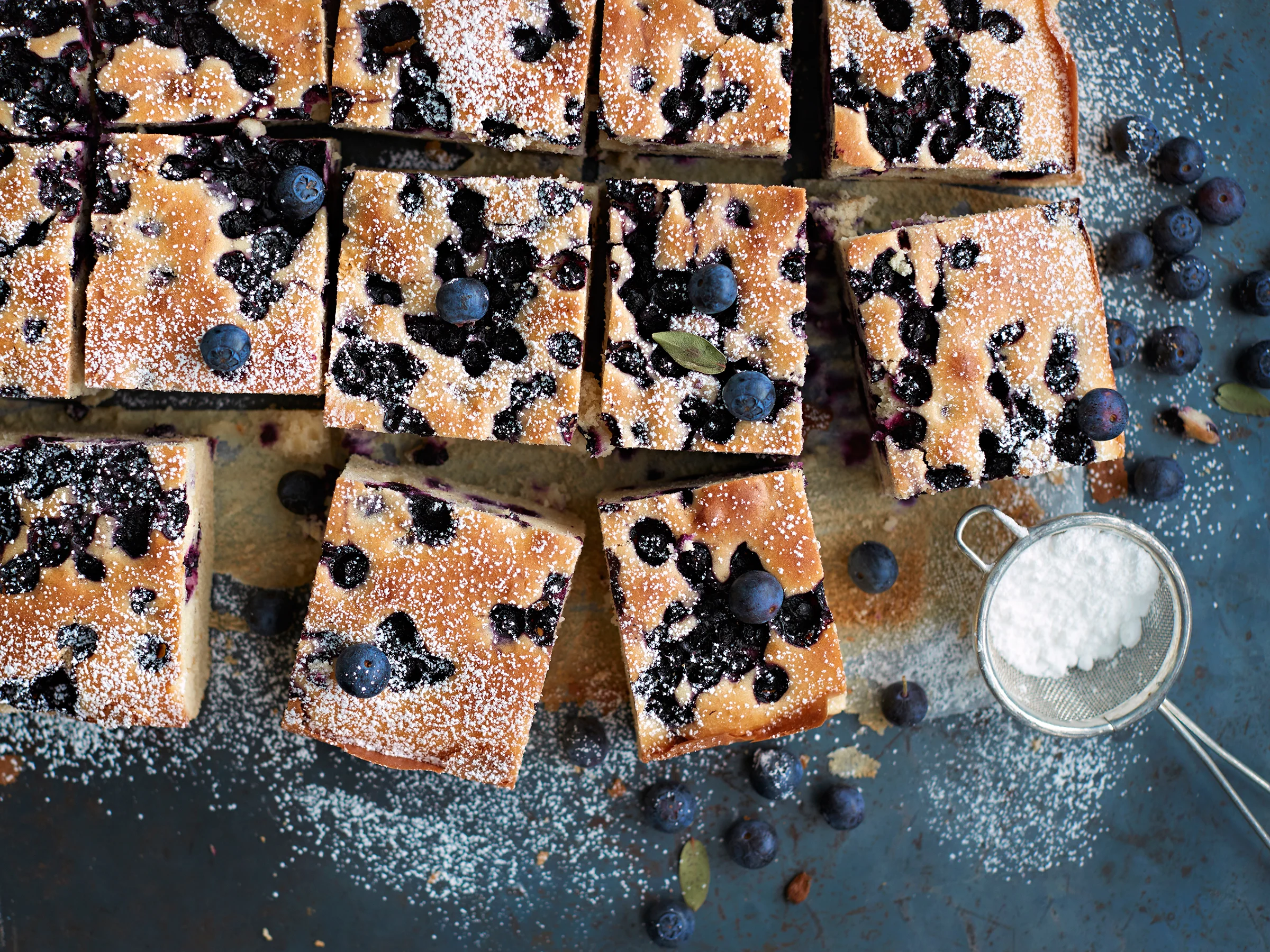 Pellillinen mustikkapiirakkaa, joka on leikattu paloiksi ja koristeltu tomusokerilla ja tuoreilla mustikoilla.