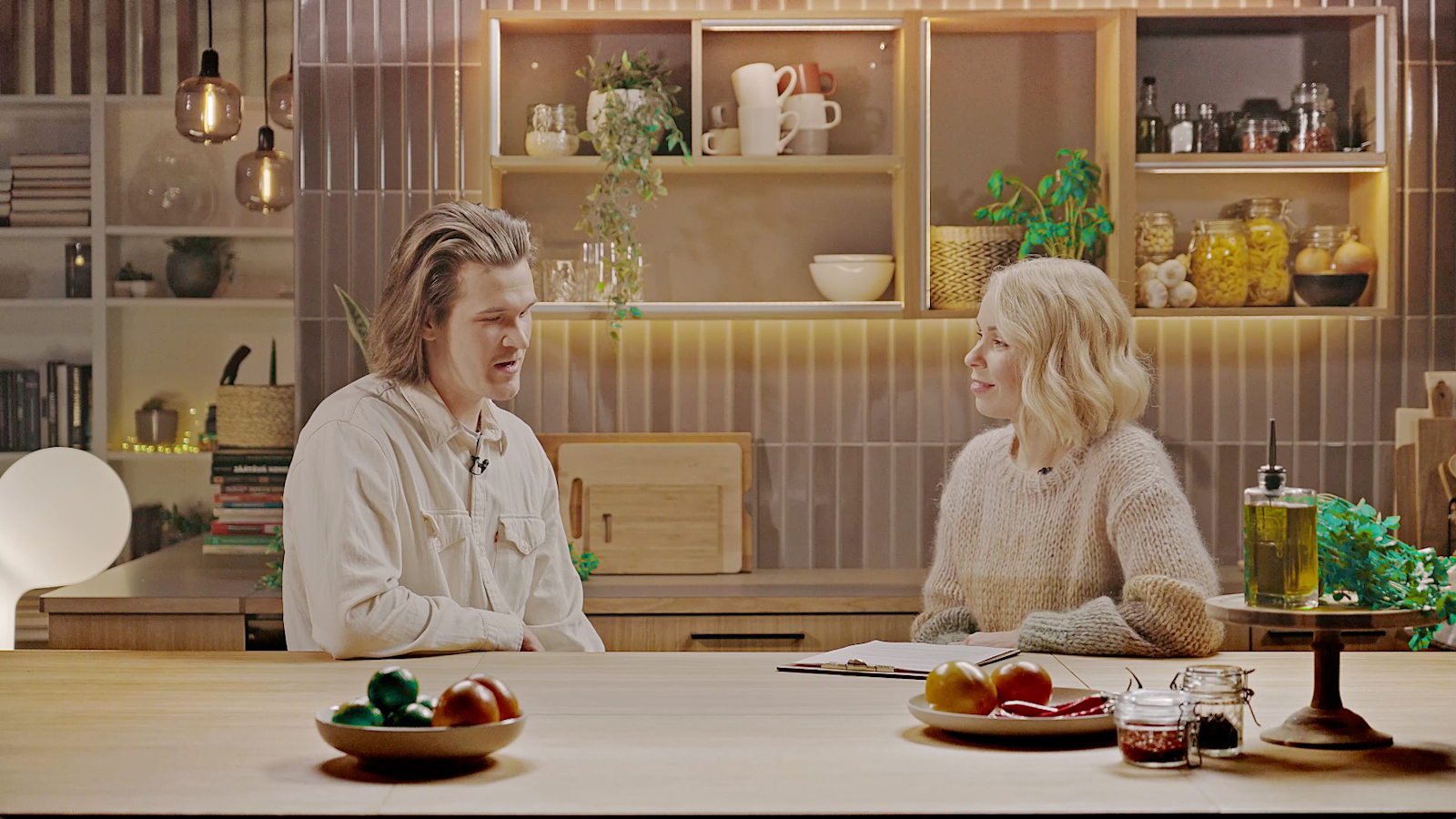 Eetu Patronen Ässästudion keittiössä toimittaja Minna Perovuon haastateltavana. Pöydällä hedelmiä. Taustalla hyllyjä, joissa muun muassa kahvikuppeja, kippoja, mausteita ja lasipurnukoita.