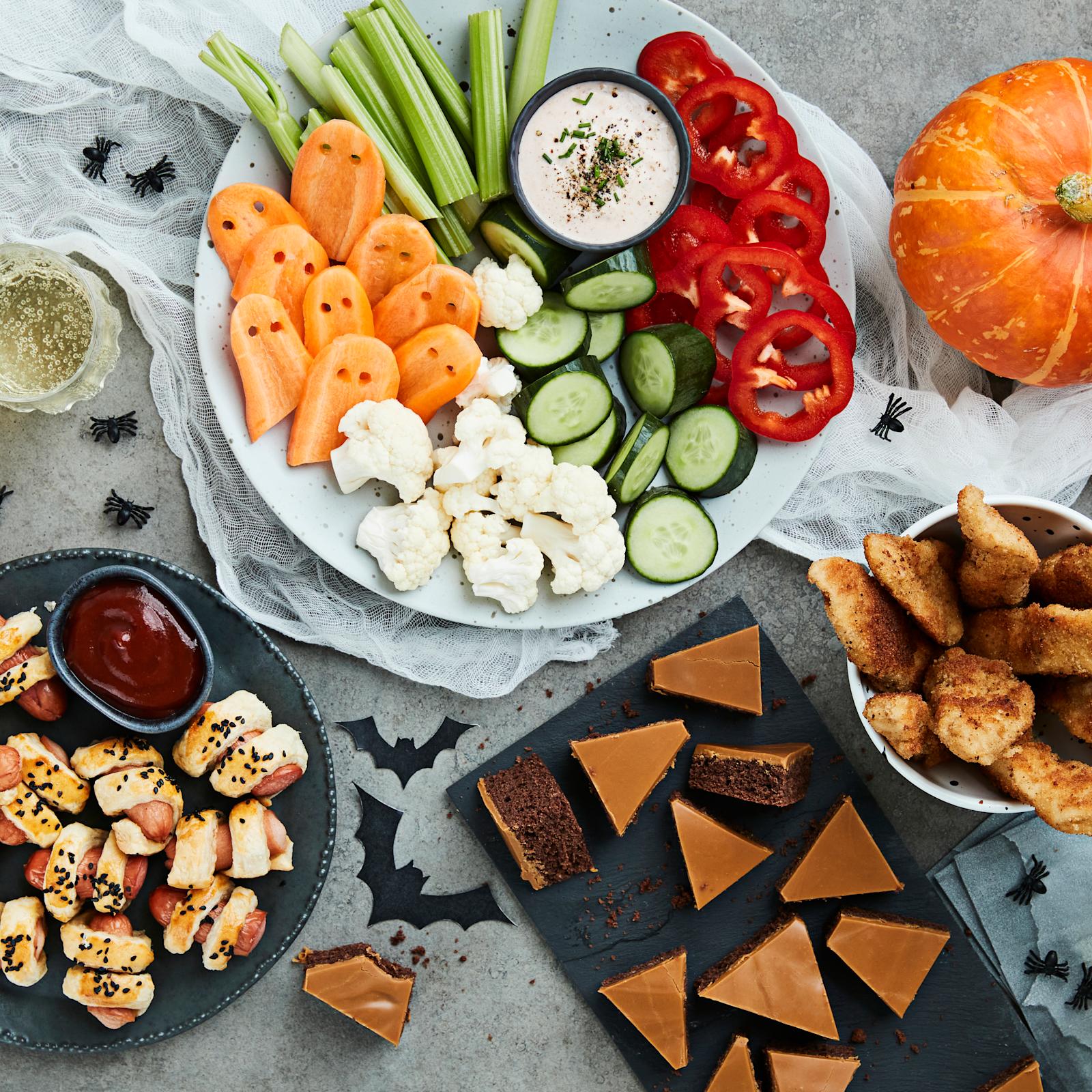 Pöytä, jolle on katettu halloween-teemaisia suolaisia ja makeita herkkuja sekä halloween koristeita.