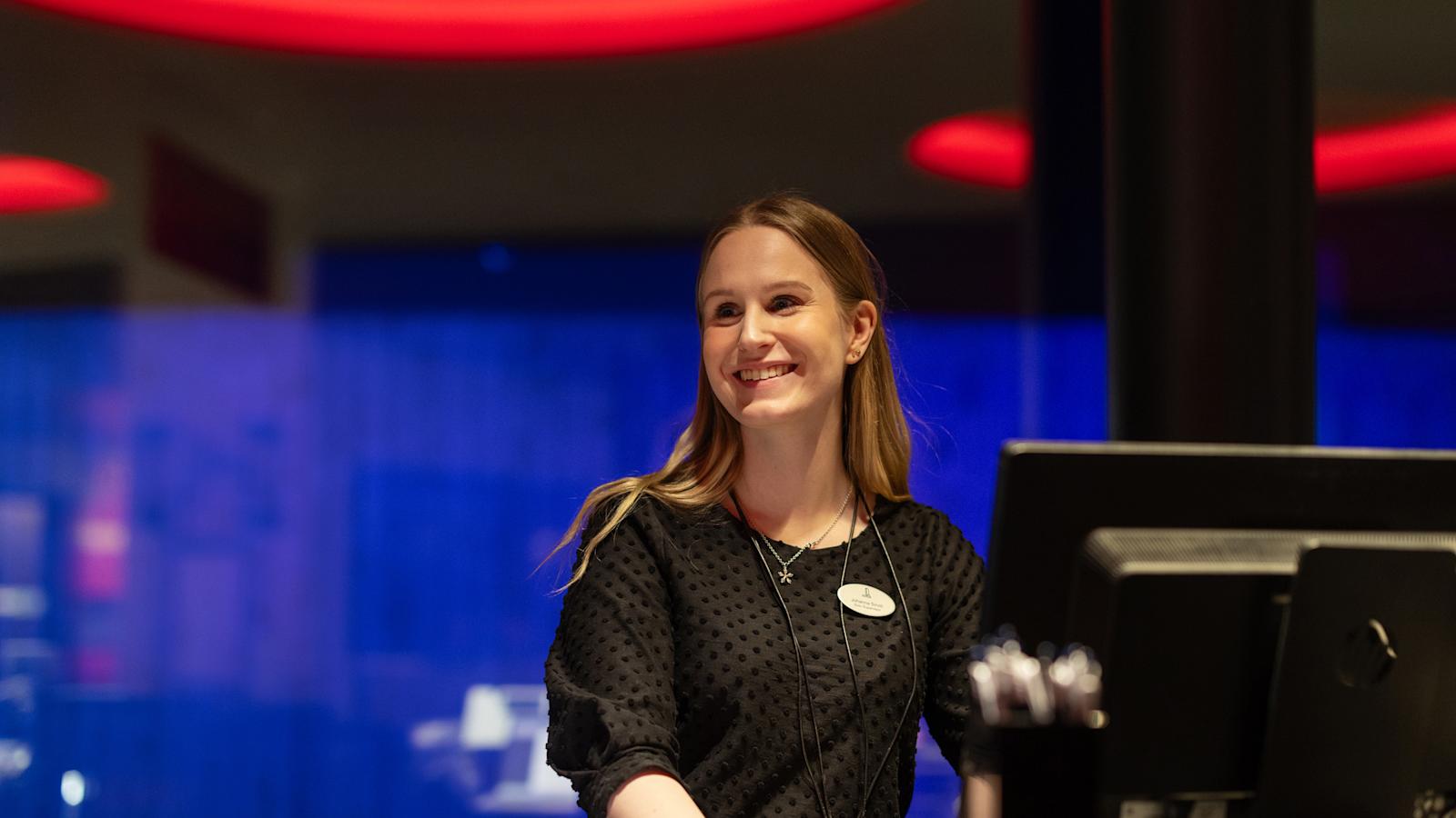 Johanna Sirviö hymyilee hotellin vastaanottotiskin takana, taustalle heijastuu valoja.