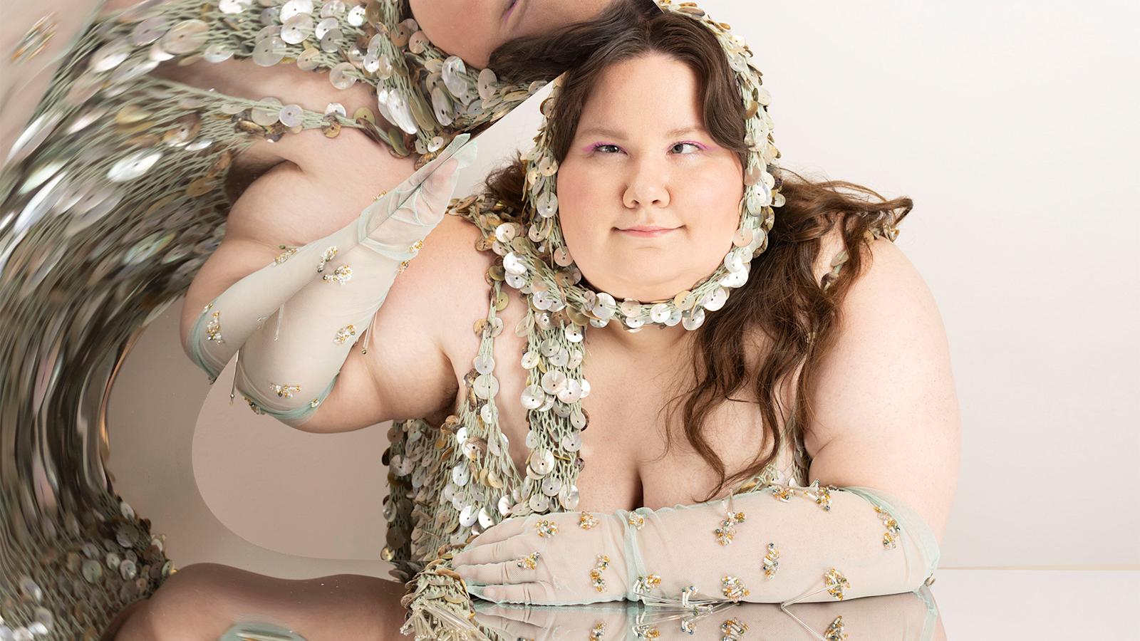 Nainen nojaa pöytään verkkomaisessa asussa.