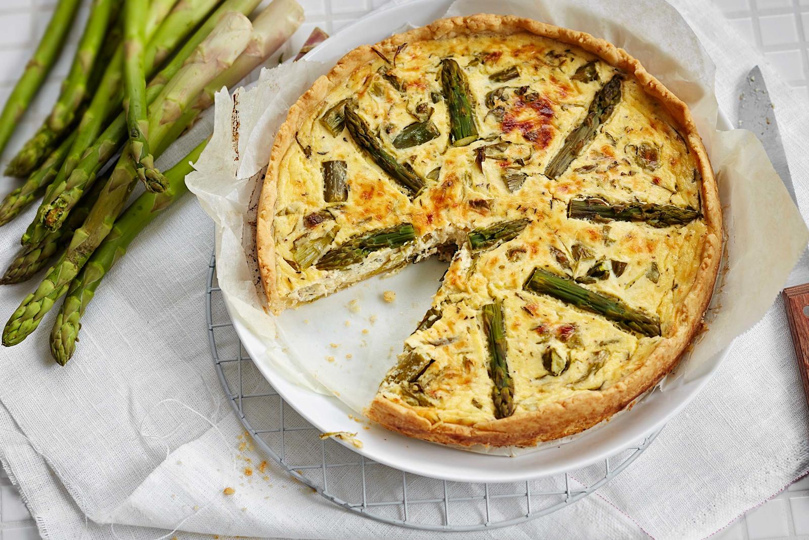 Pöydällä parsa-rucolapiirakka sekä nippu tuoreita parsoja.