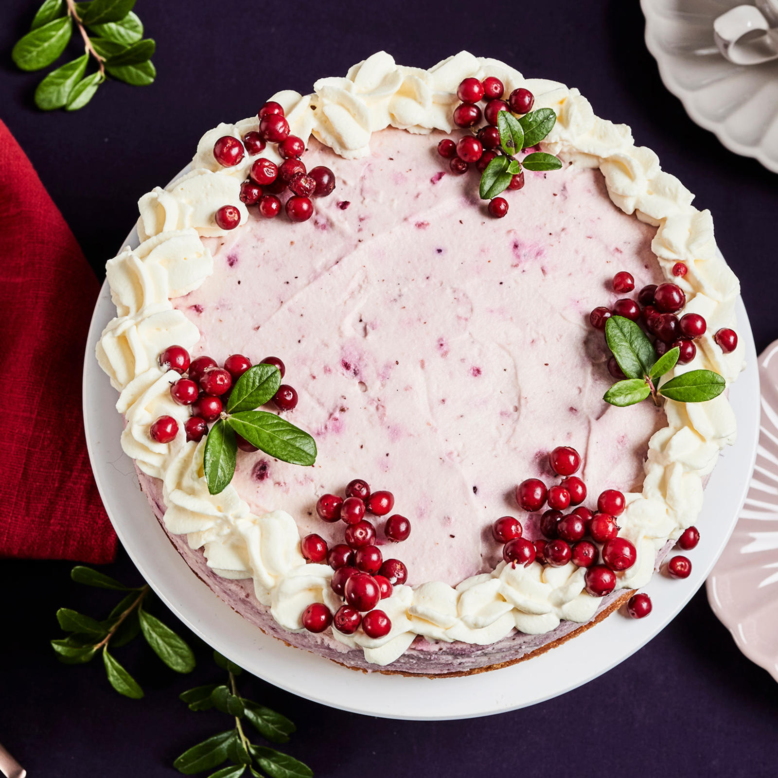 Puolukkamoussekakku, jonka vieressä kaksi kakkulautasta, kahvikuppi ja punainen liina.