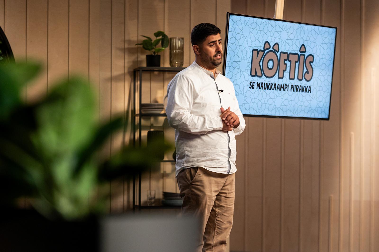 Siva Parlar seisoo ison näytön edessä. Näytöllä lukee Köftis.
