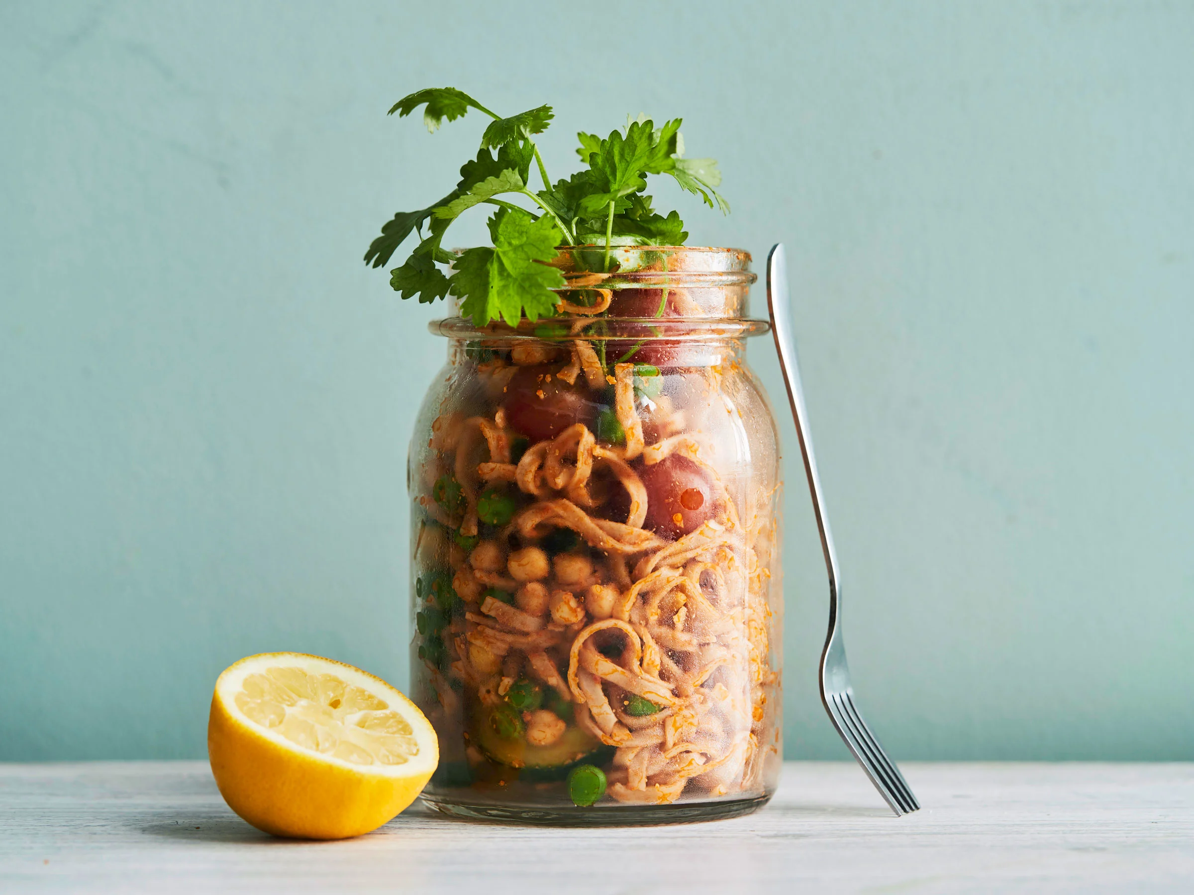 Kiinalainen purkkiherkku annosteltuna isoon lasipurkkiin. Päällä korianterin lehtiä ja vieressä puolikas sitruuna. Purkkia vasten nojaa haarukka.