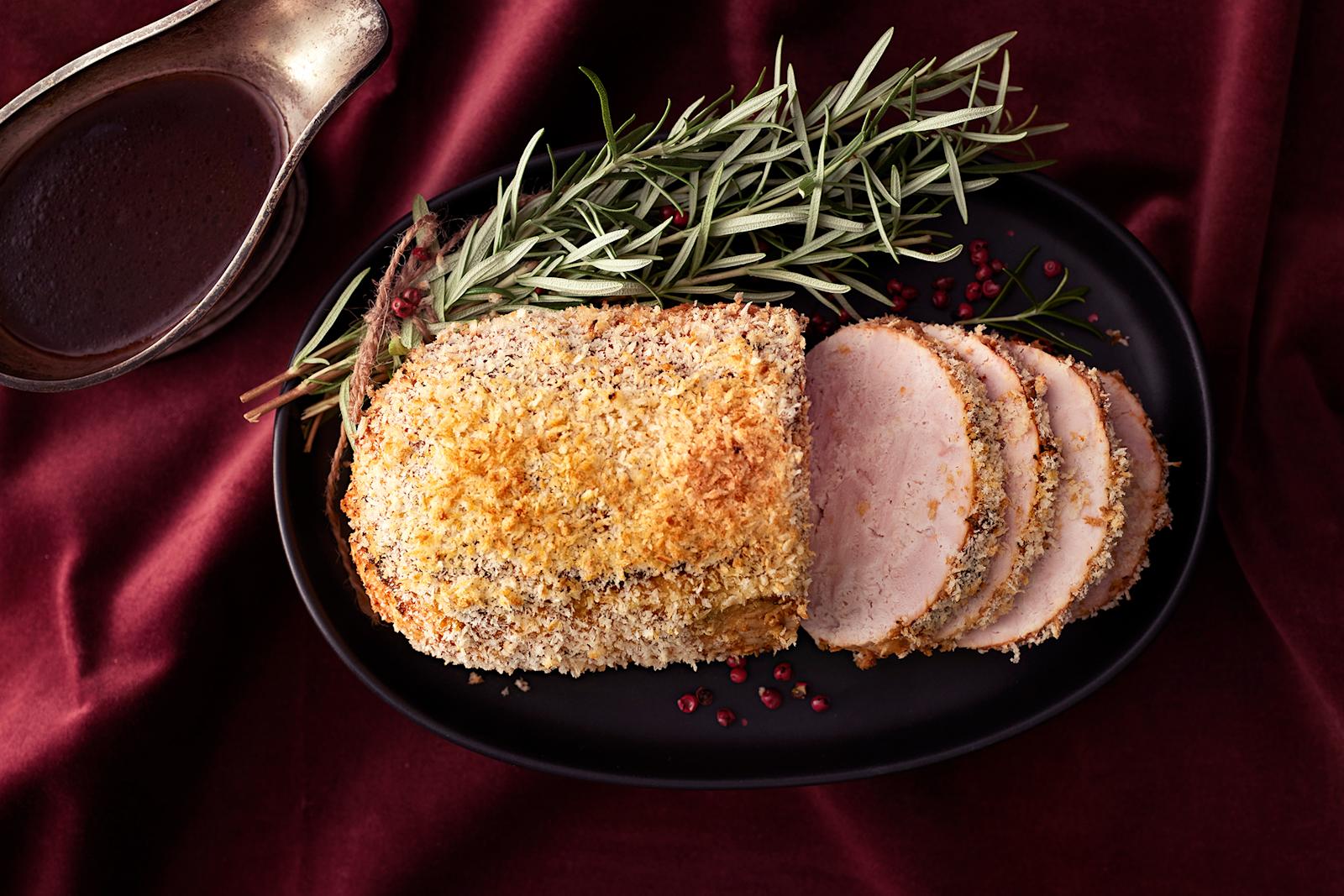 Kalkkunarulla, josta leikattu viipaleita tarjoiluastialle. Tarjoiluastian reunalla koristeena rosmariinin oksia. Vieressä punaviinikastiketta kastikekulhossa.