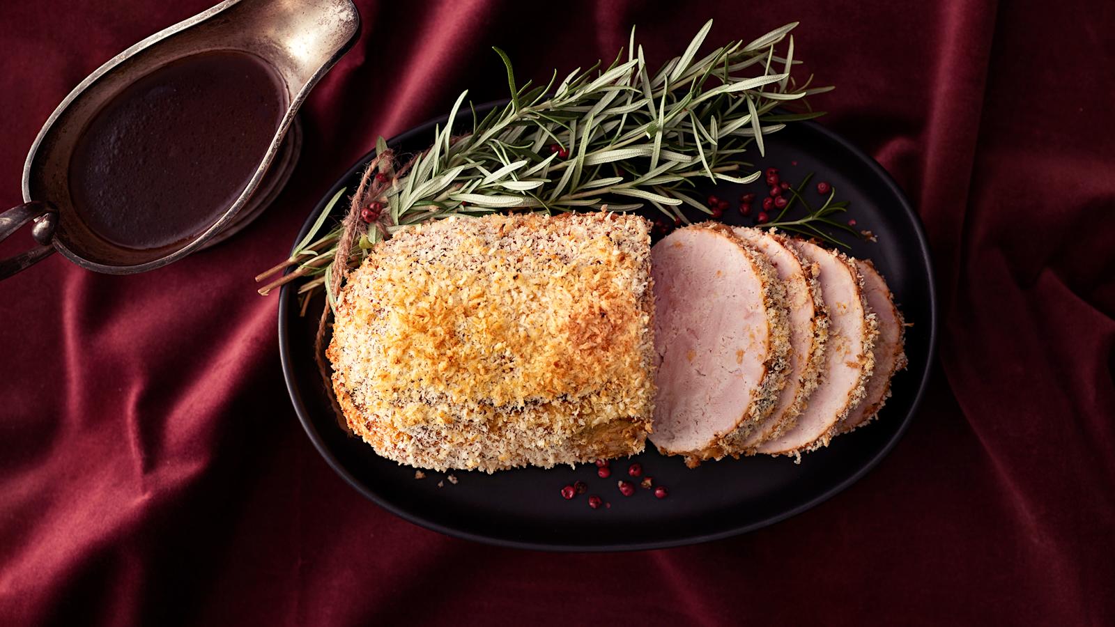 Kalkkunarulla, josta leikattu viipaleita tarjoiluastialle. Tarjoiluastian reunalla koristeena rosmariinin oksia. Vieressä punaviinikastiketta kastikekulhossa.