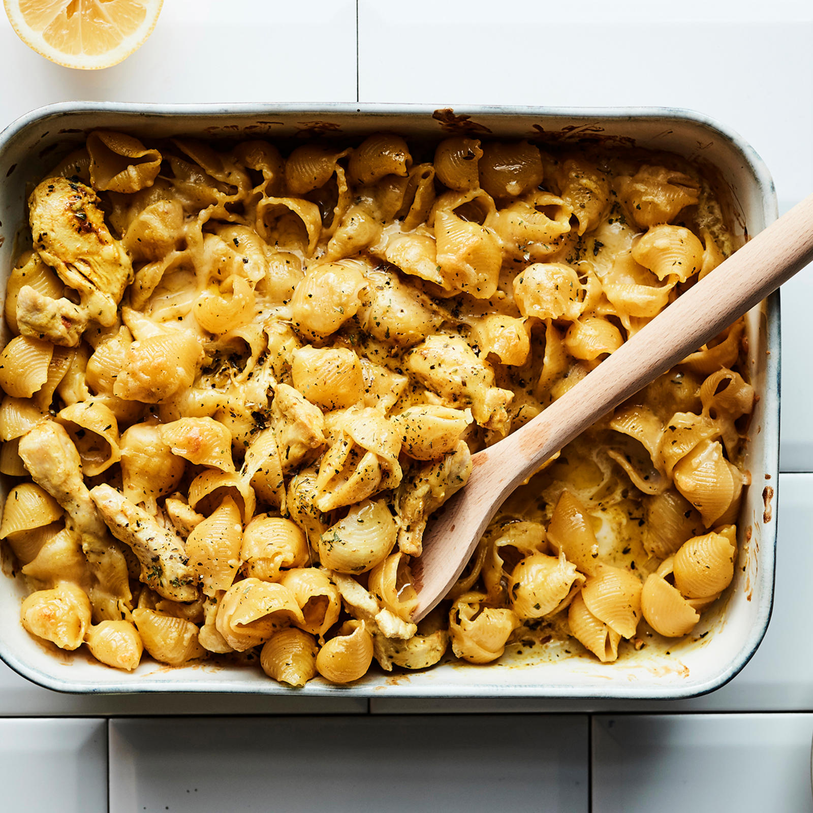 Uunivuoka, jossa Palermon kanapastaa sekä puinen otin. Vieressä puinen sitruspuserrin ja puolikas sitruuna lasilautasella, sekä valkoinen ruokalautanen ja lautasliinan kulma.