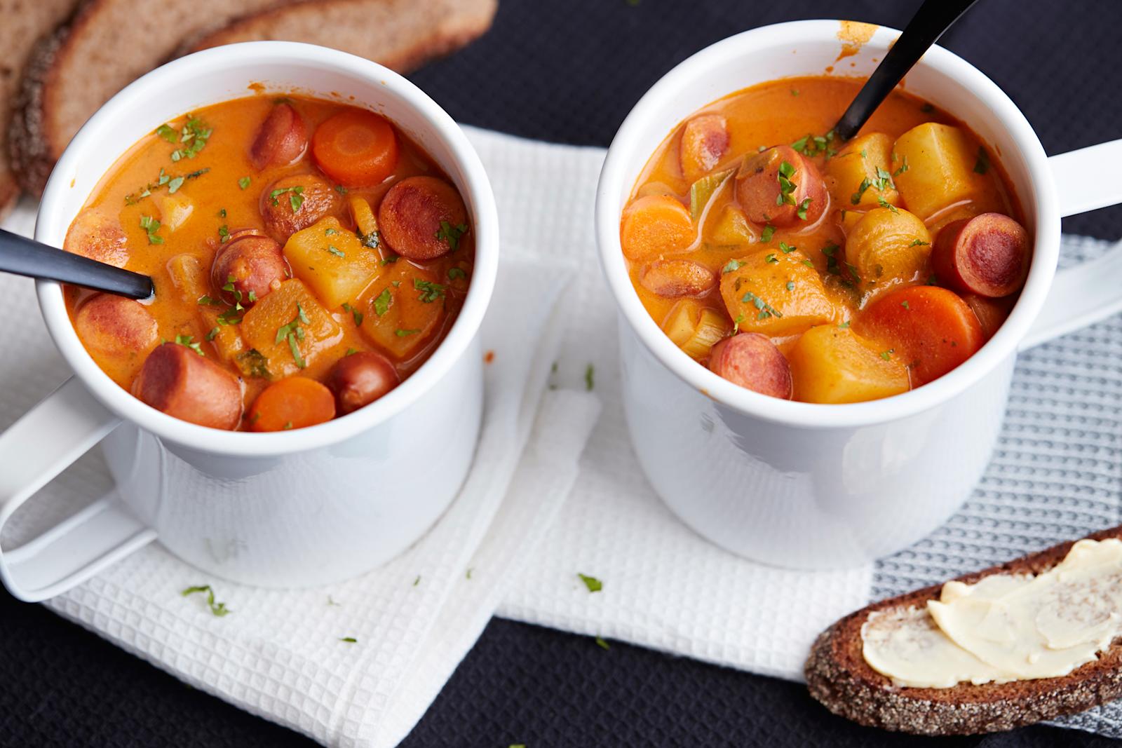 Nakkikeittoa kahdessa isossa mukissa, joissa lusikat. Mukien alla vaalea liina. Vieressä ruisleipäviipaleita.