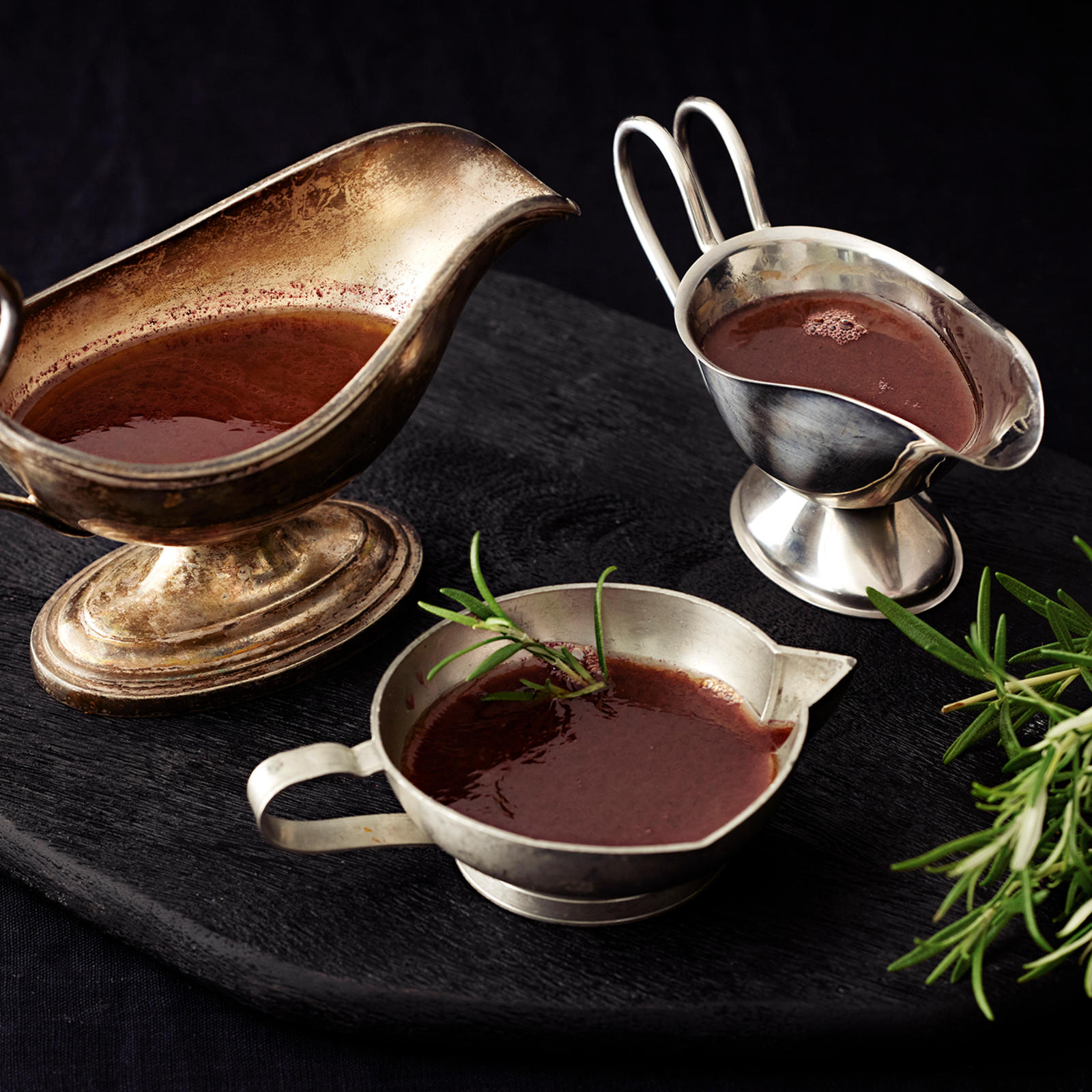 Rosmariini-punaviinikastiketta kolmessa kastikekannussa. Kannujen vieressä rosmariinin oksa.