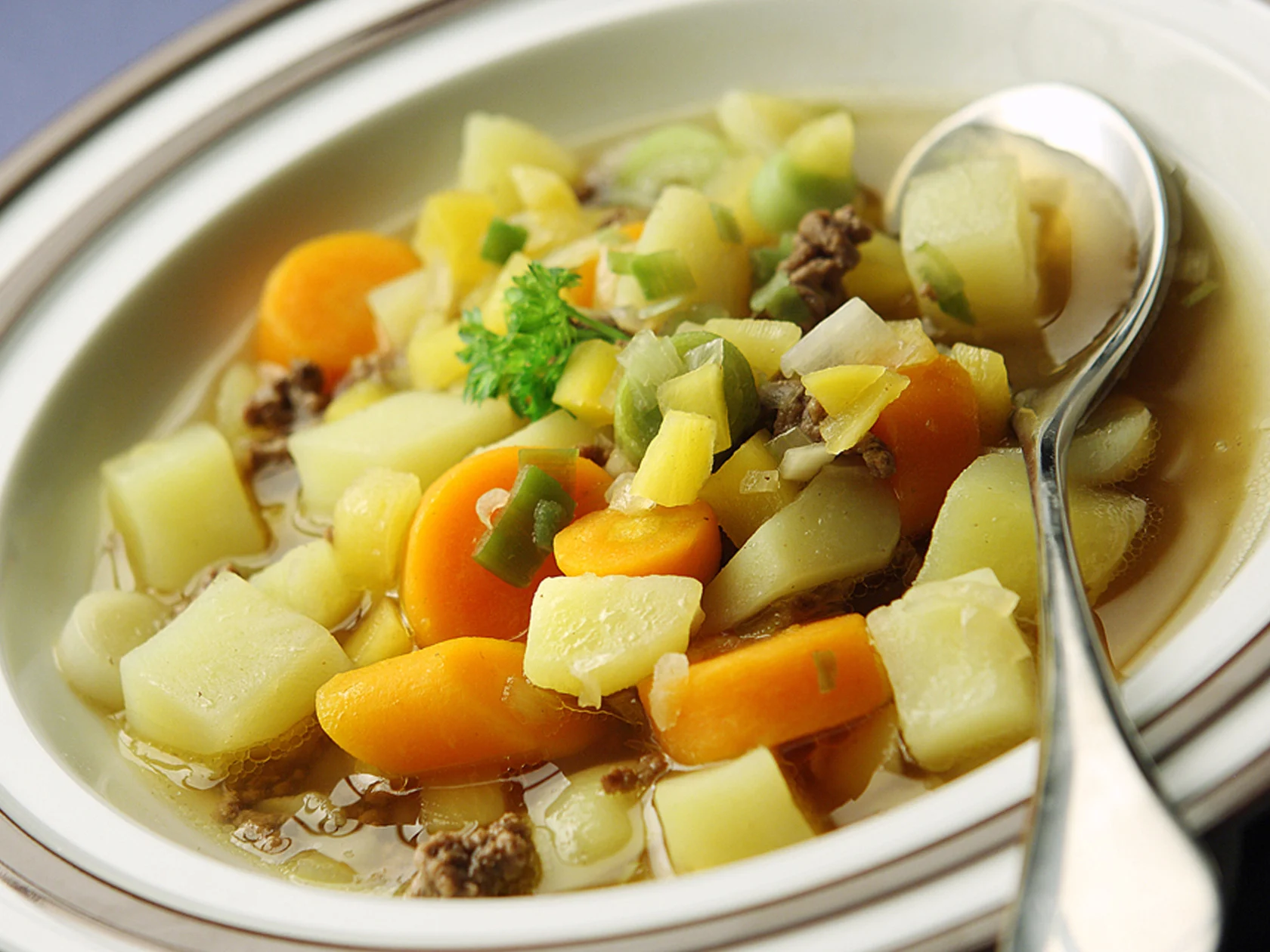 Syvä lautanen, jossa jauhelihakeittoa ja ruokalusikka.