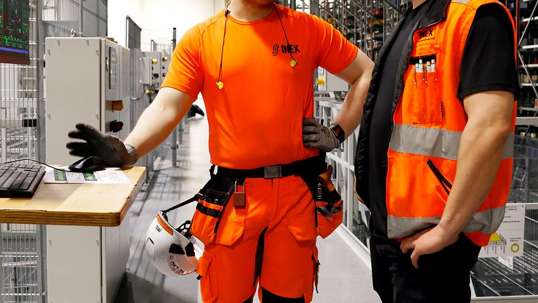 Kaksi työasuun pukeutunutta miestä juttelee logistiikkakeskuksessa