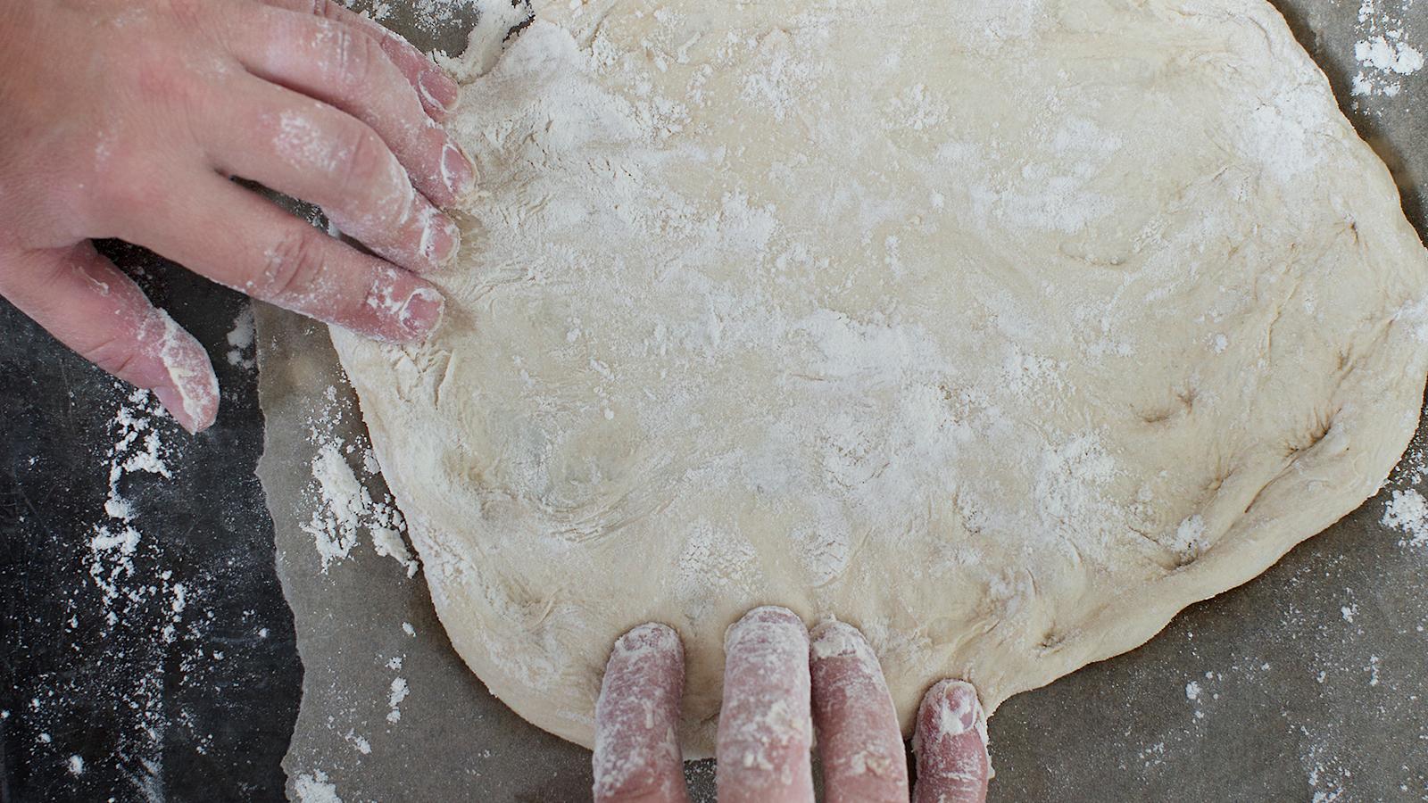 3\. Säädä uuni 250 asteeseen. Muotoile pohja jauhotetulla alustalla käsin, älä kauli. Tee pellillinen tai pienempiä pizzoja. Painele pohja aitoon napolilaiseen tyyliin taikinapalan keskeltä kohti reunoja, korkeintaan kolmen millin paksuiseksi.