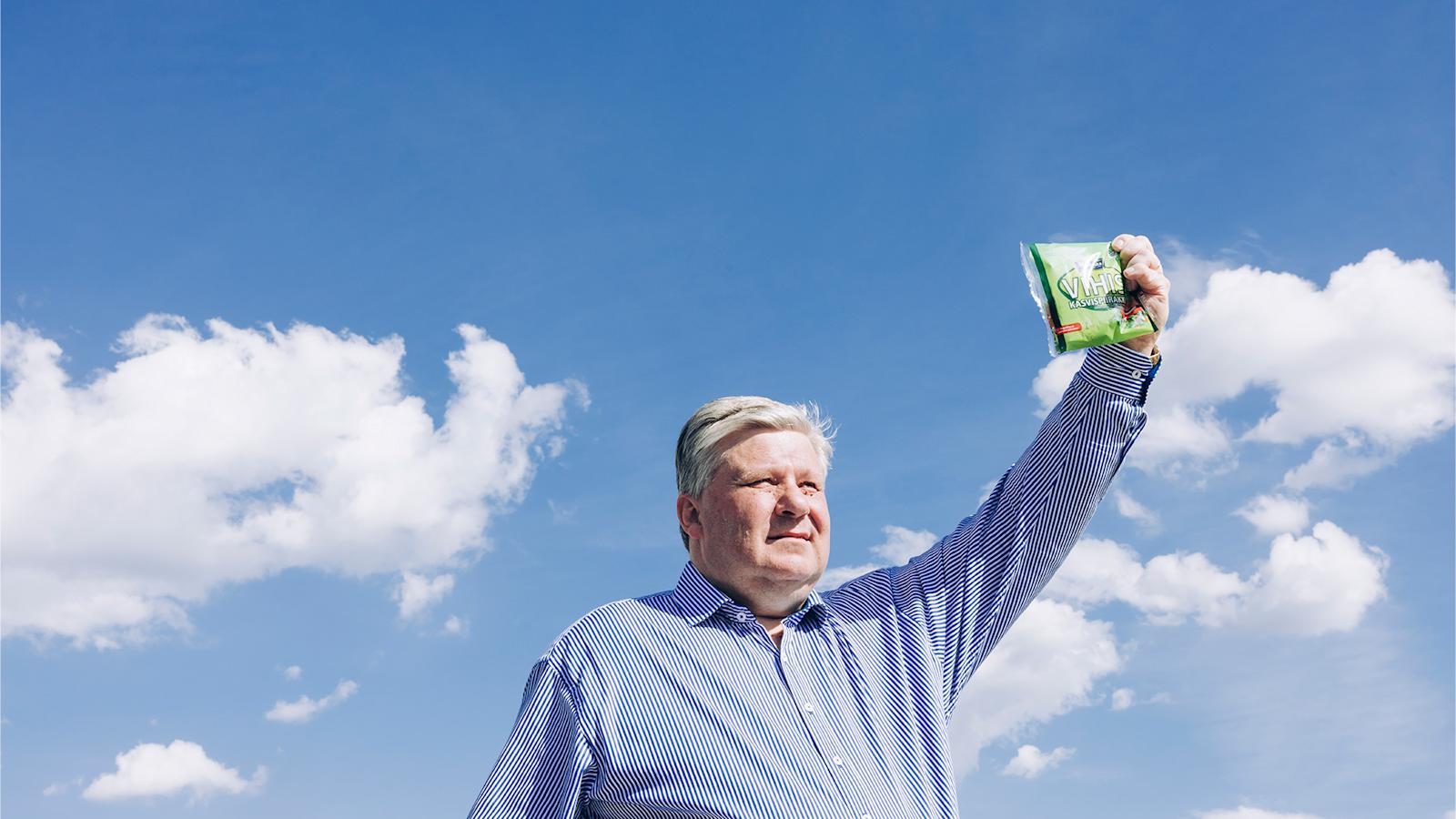 Mies kohottaa kädessään olevan Vihis-piirakkapakkauksen kohti pilvistä taivasta