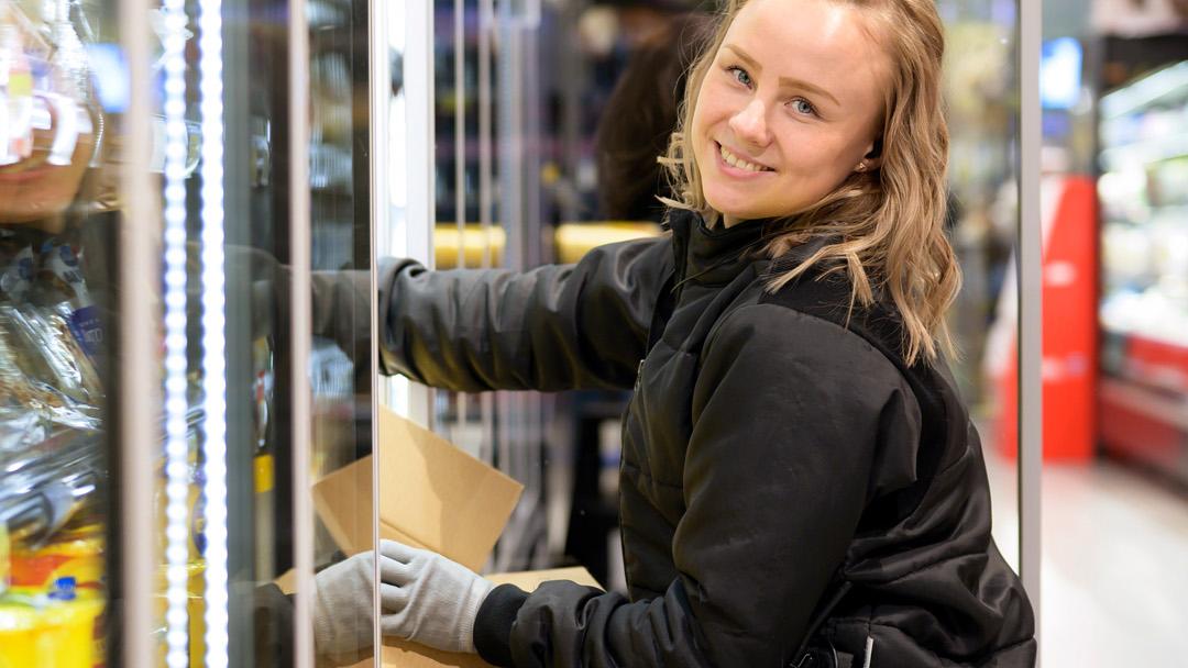 Kati Kuuliainen täyttää kylmäkaappia kameralle hymyillen.
