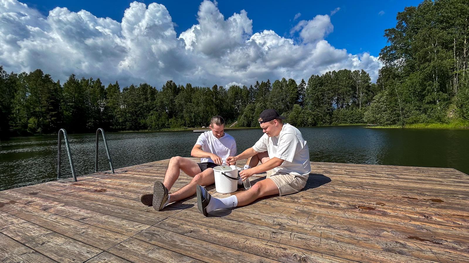 Kaksi miestä istuu laiturilla. He lusikoivat ämpäristä vettä pulloihin.
