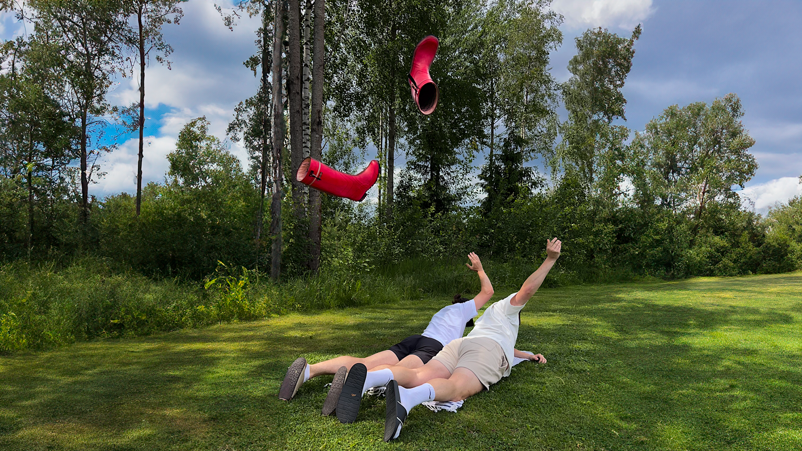 kaksi miestä vatsallaan ruohikolla. Heittävät kumisaapasta selän yli.