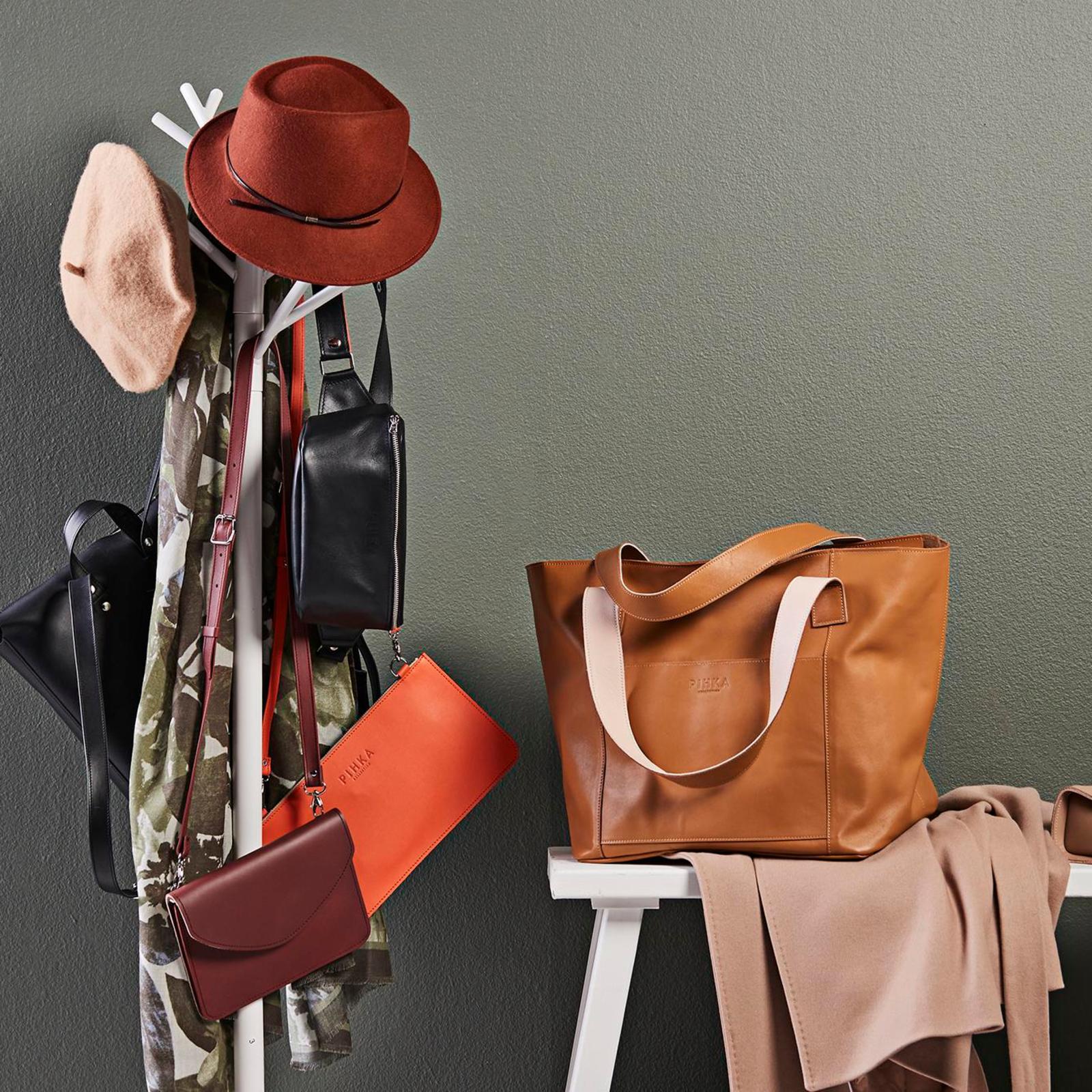 Pihkan laukkumalleja roikkuu valkoisessa naulakossa.