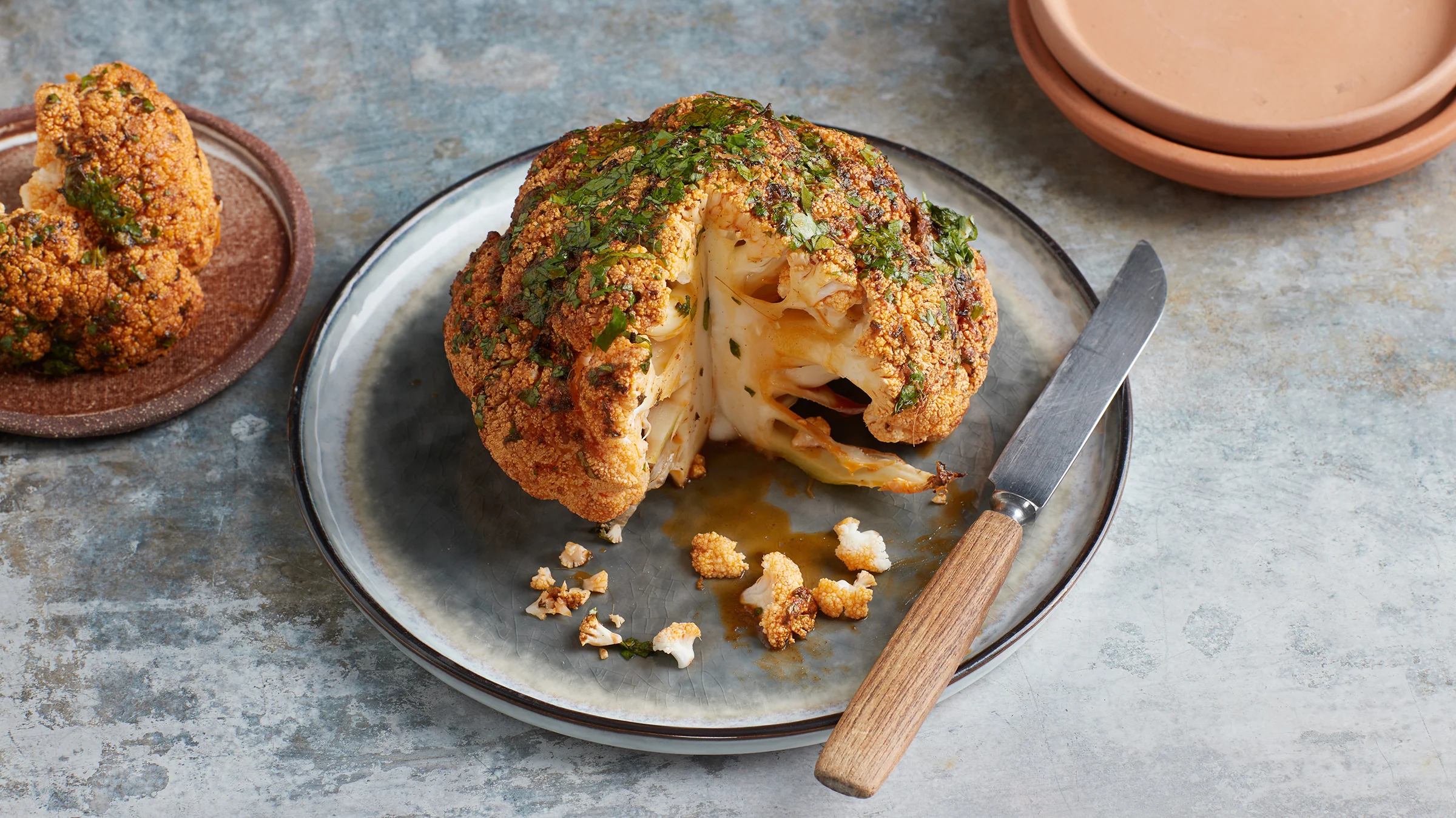 Kokonainen kukkakaali uunissa valmistettuna. Kaalin vieressä veitsi ja lautanen, jolle leikattu pala kaalia.