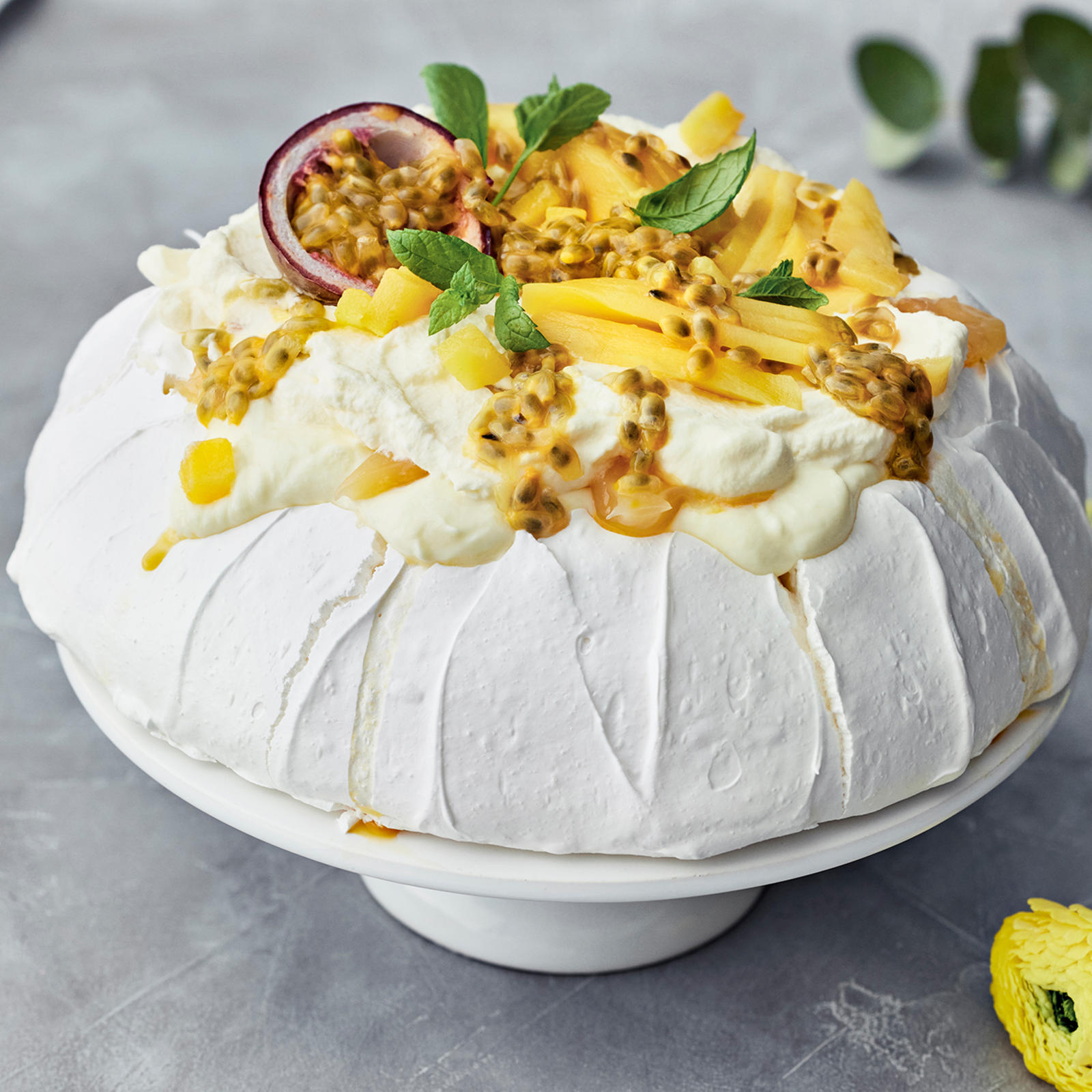 Pavlova joka on koristeltu passionhedelmällä, mangolla ja mintunlehdillä.