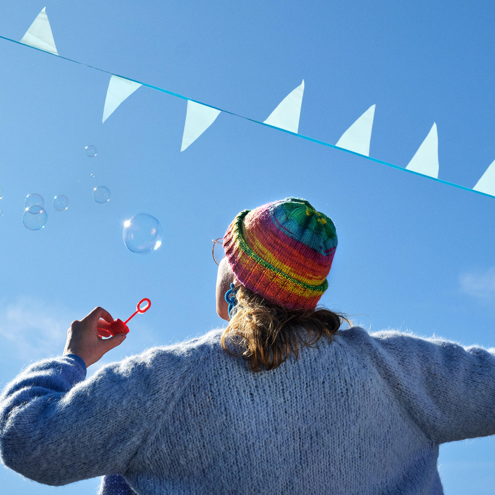 Sateenkaarenvärinen pipo päässään oleva henkilö, joka puhaltaa saippuakuplia.