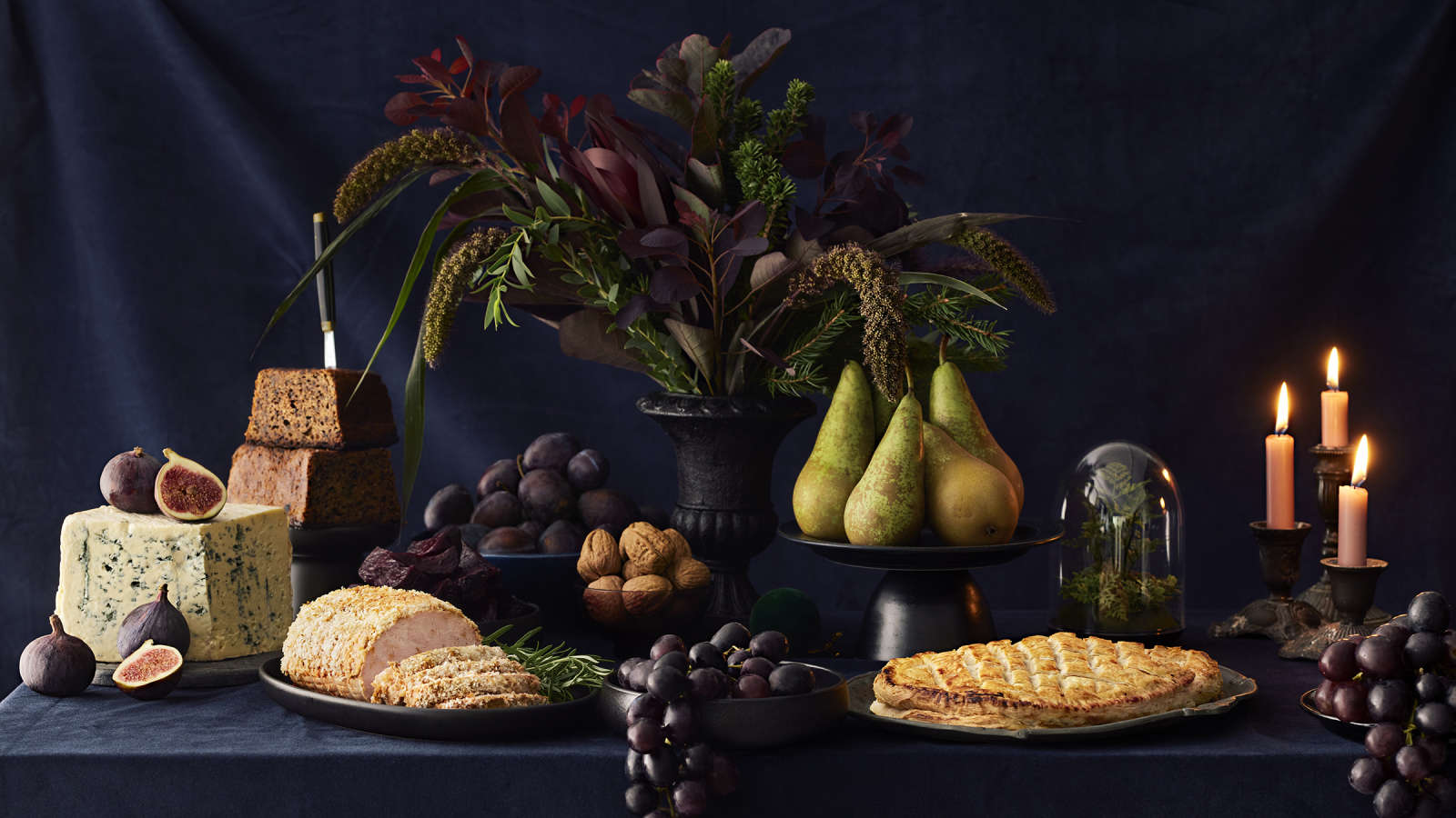 Jouluinen kattaus, jossa kalkkunarulla, vegaaninen Wellington, saaristolaisleipä, hedelmiä, pähkinöitä, juustoja, kynttilöitä ja kukka-asetelma
