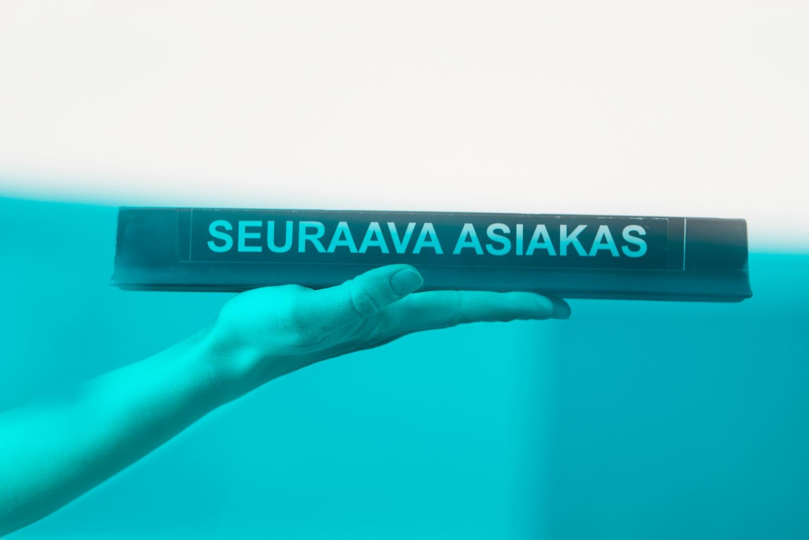 Käsi, joka kannattelee Seuraava asiakas -kylttiä