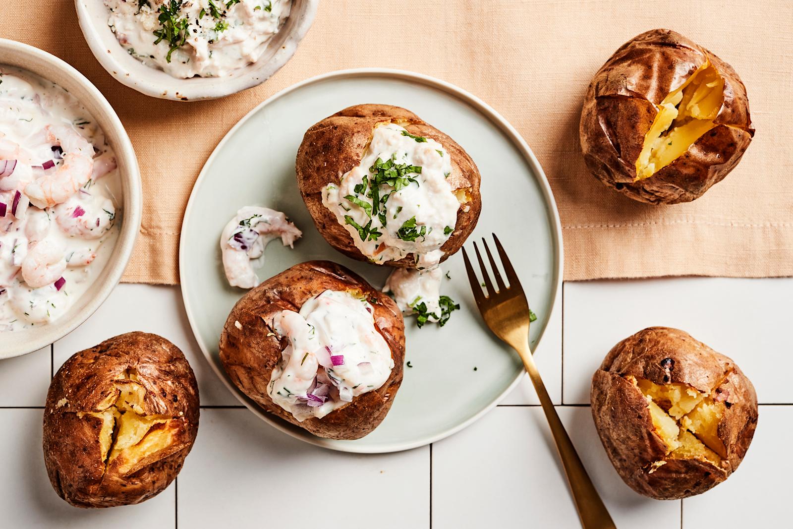 Viisi uuniperunaa, joista kaksi lautasella katkarapu- ja kanatäytteellä täytettynä. Lautasella haarukka ja lautasen vieressä täytteitä kulhoissa.