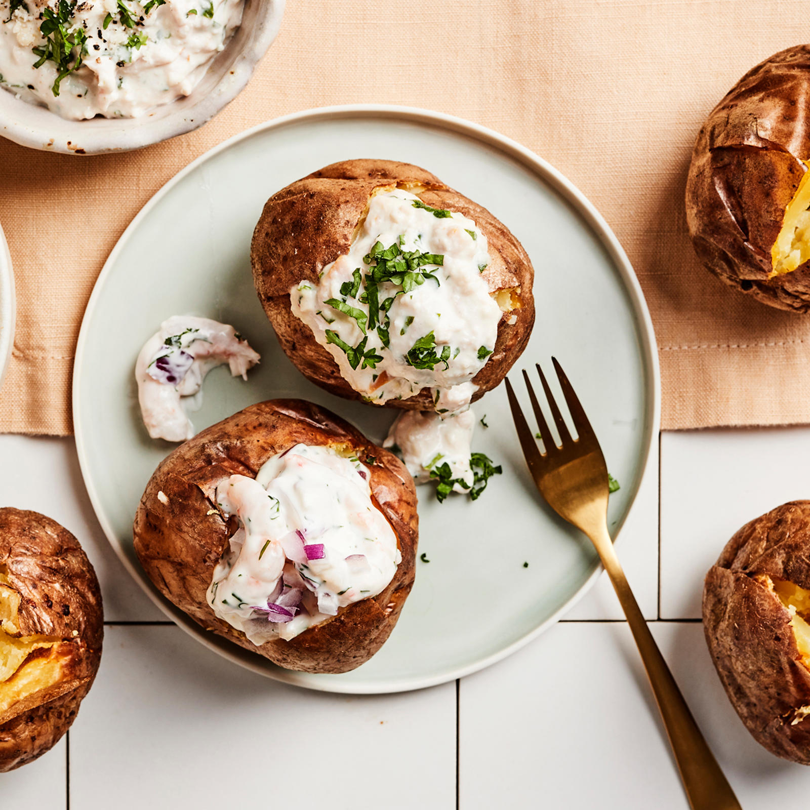 Viisi uuniperunaa, joista kaksi lautasella katkarapu- ja kanatäytteellä täytettynä. Lautasella haarukka ja lautasen vieressä täytteitä kulhoissa.