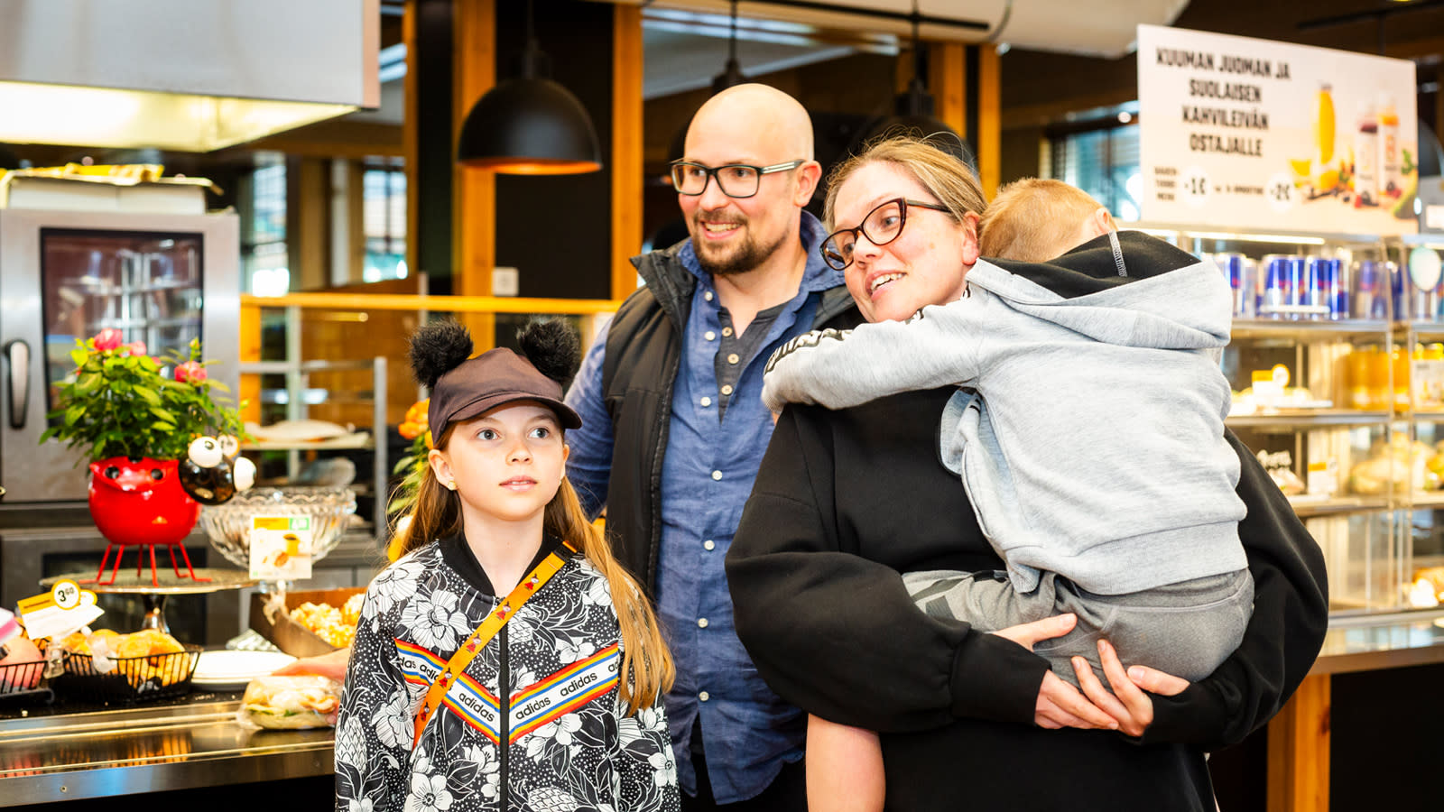 Perhe huoltoasemalla. Pieni poika on äitinsä sylissä, tytär seisoo isänsä vieressä.