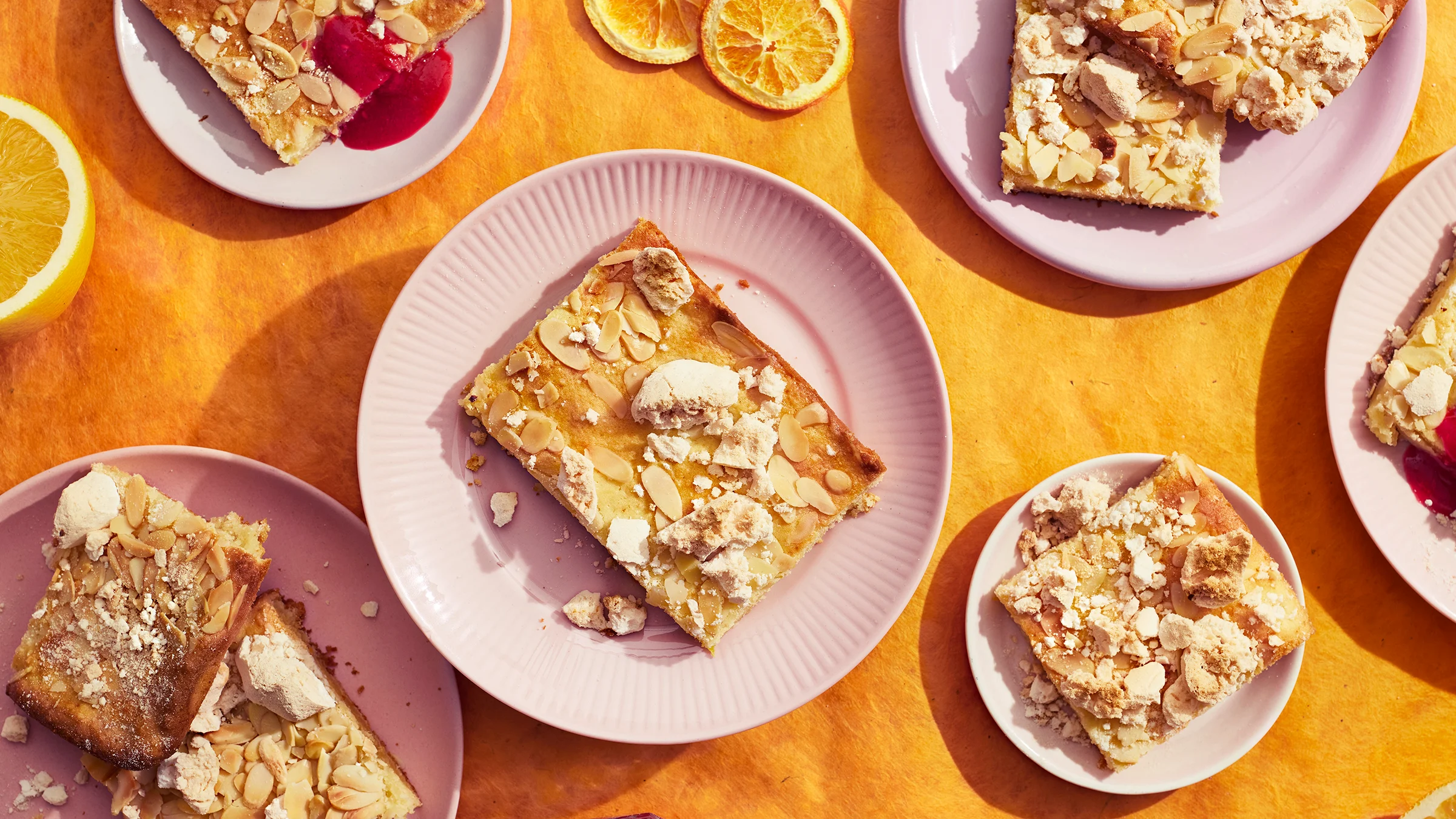 Appelsiini-tuorejuustopaloja vaaleanpunaisilla lautasilla. Lautasten alla oranssi liina ja vieressä appelsiinisiivuja.