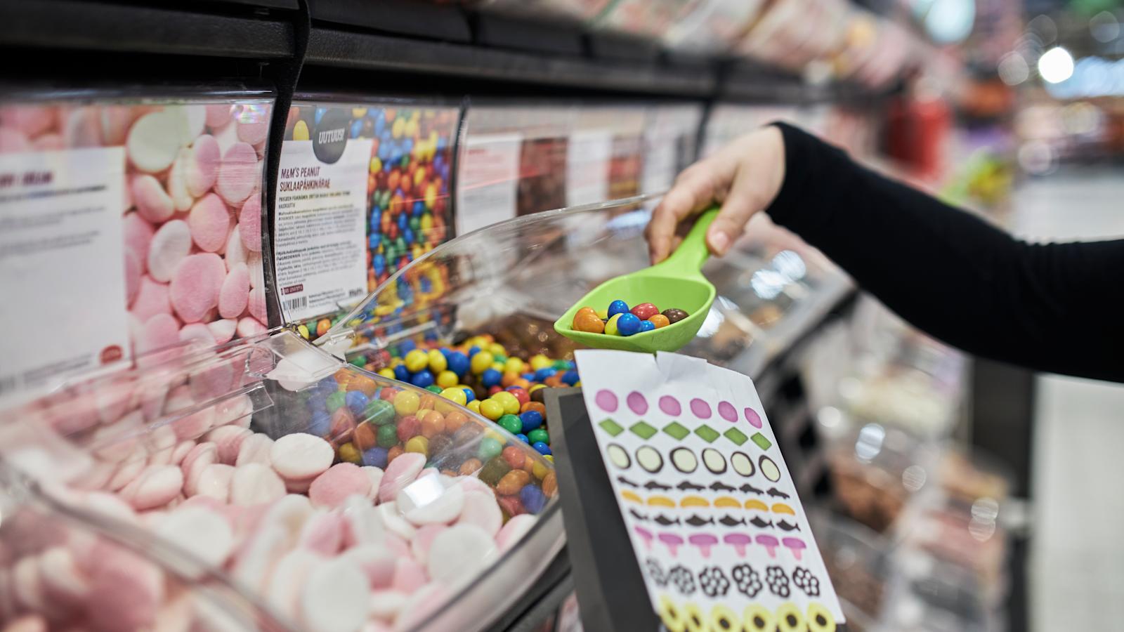 Henkilö ottamassa kauhalla irtokarkkeja paperiseen irtokarkkipussiin.